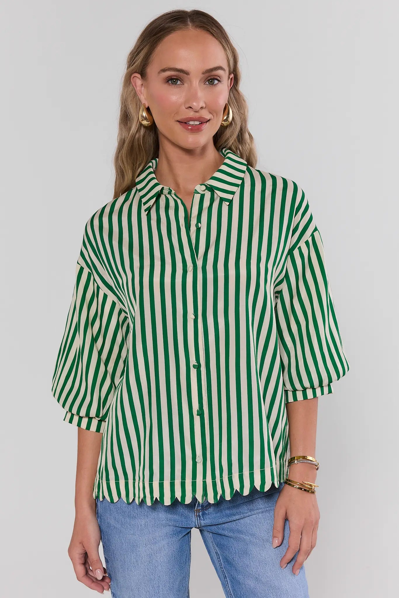 Woman wearing a green and white striped shirt with blue jeans on a plain background