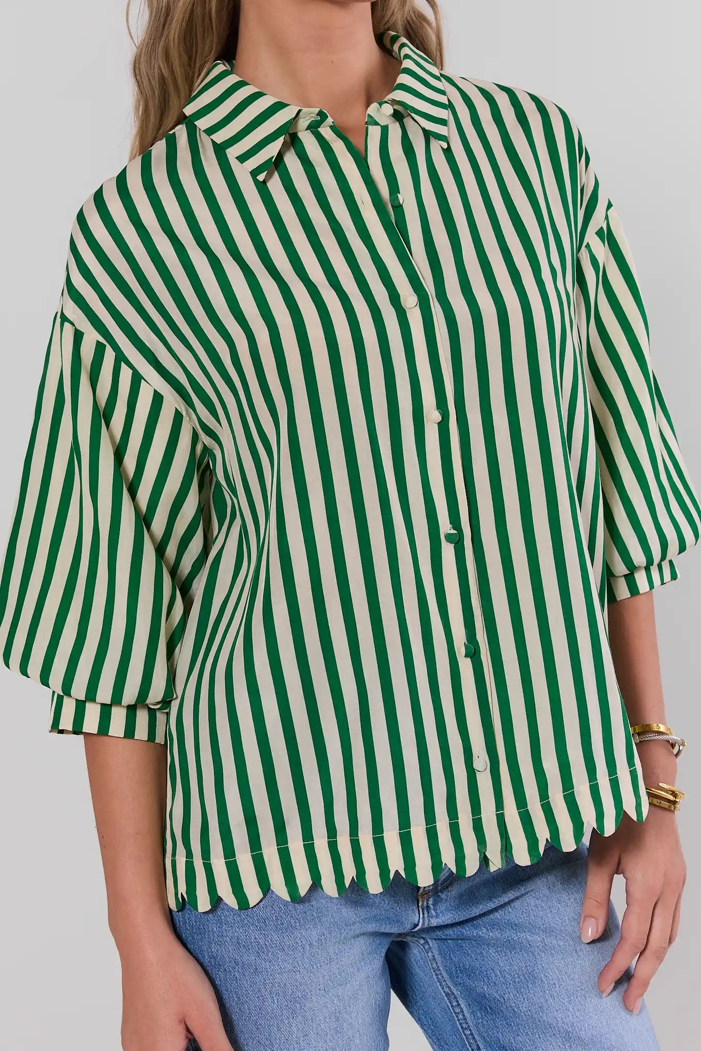 Person wearing a green and white striped shirt with blue jeans on a plain background close up