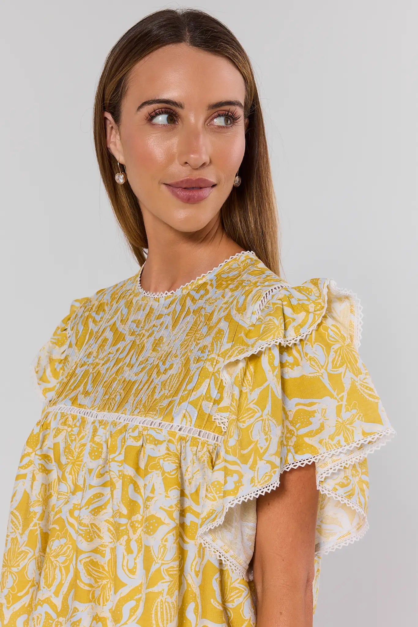 Woman wearing a yellow floral top against a plain background close up