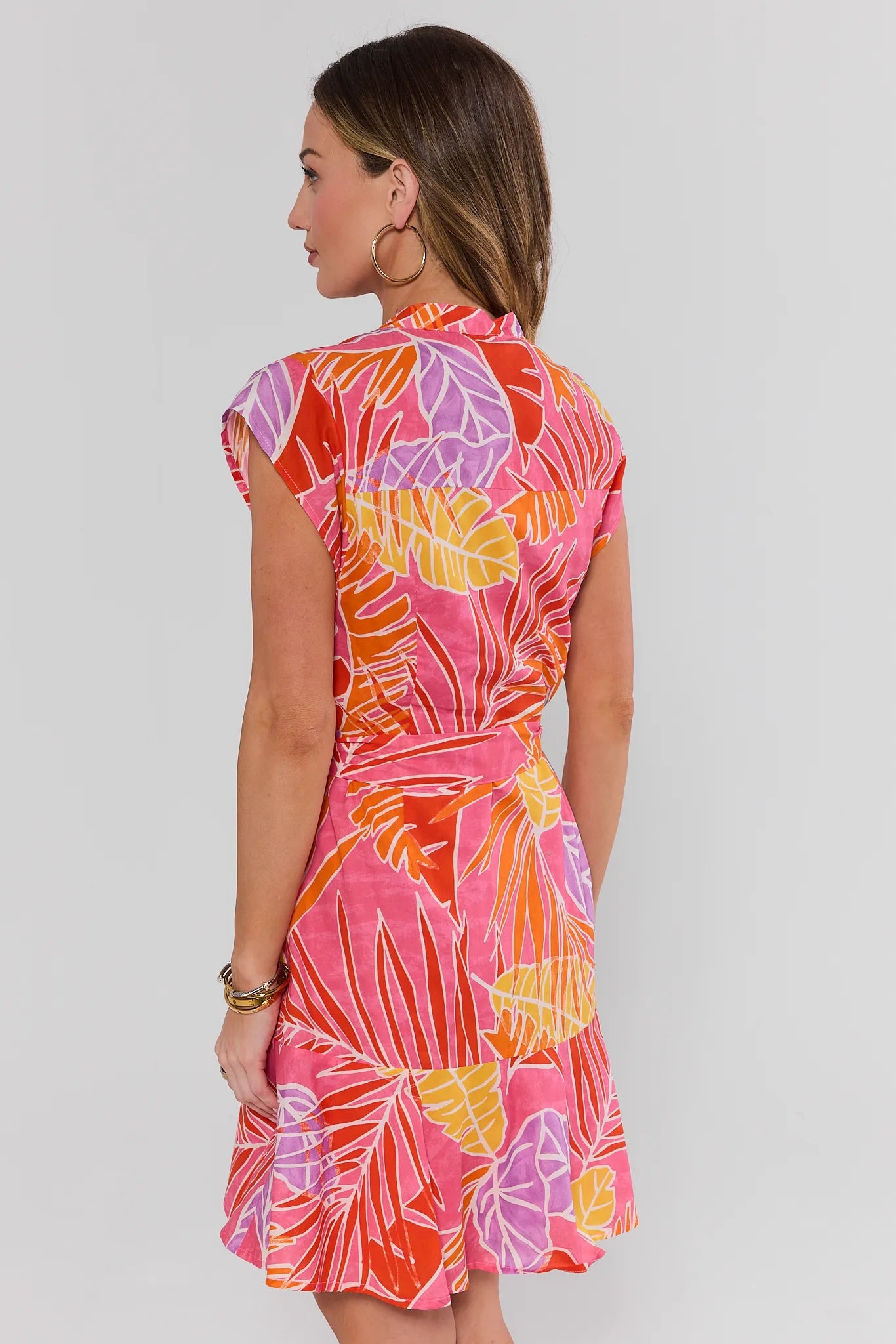 Woman wearing a colorful dress with a leaf pattern on a plain background stand