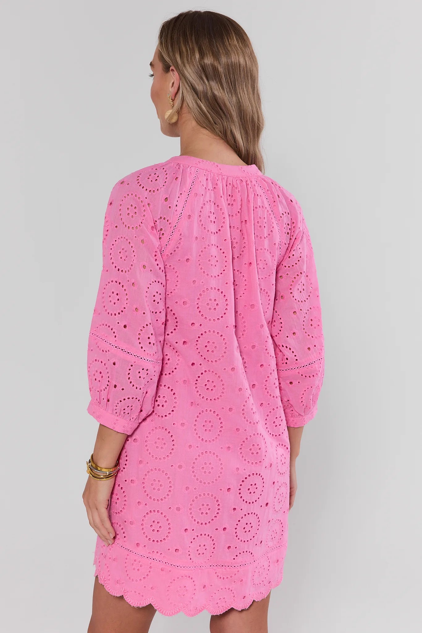 Woman wearing a pink lace dress against a plain background stand