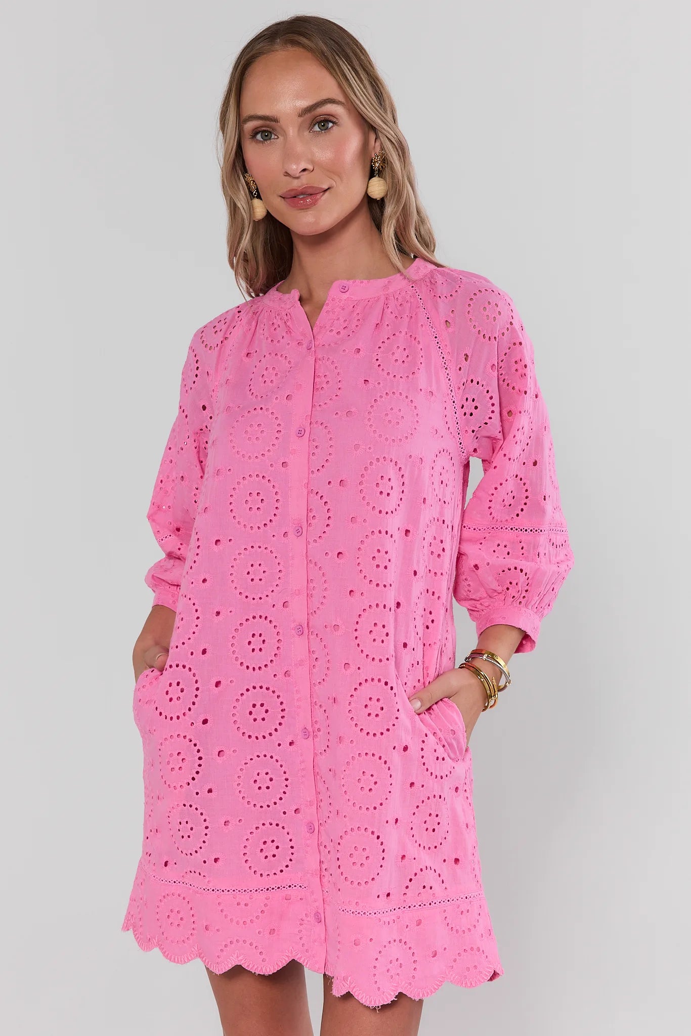 Woman wearing a pink dress with intricate cut-out patterns on a plain background side