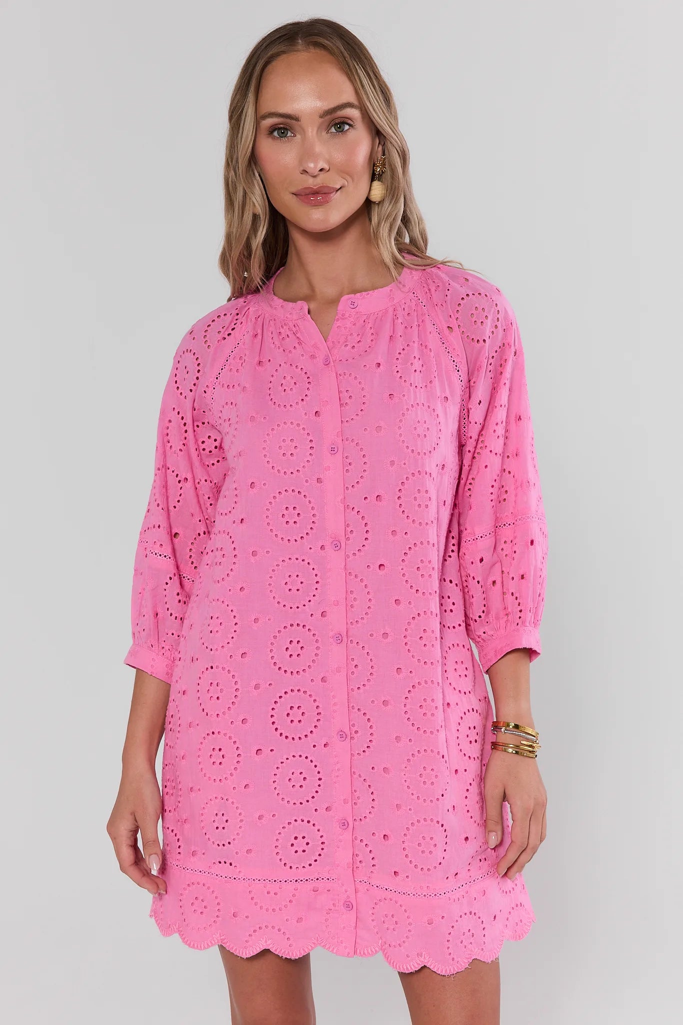 Woman wearing a pink lace dress against a plain background standing