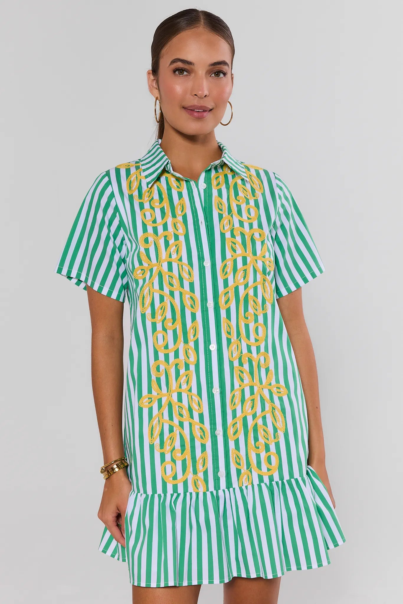 Woman wearing a green and white striped dress with yellow embroidery on a plain background