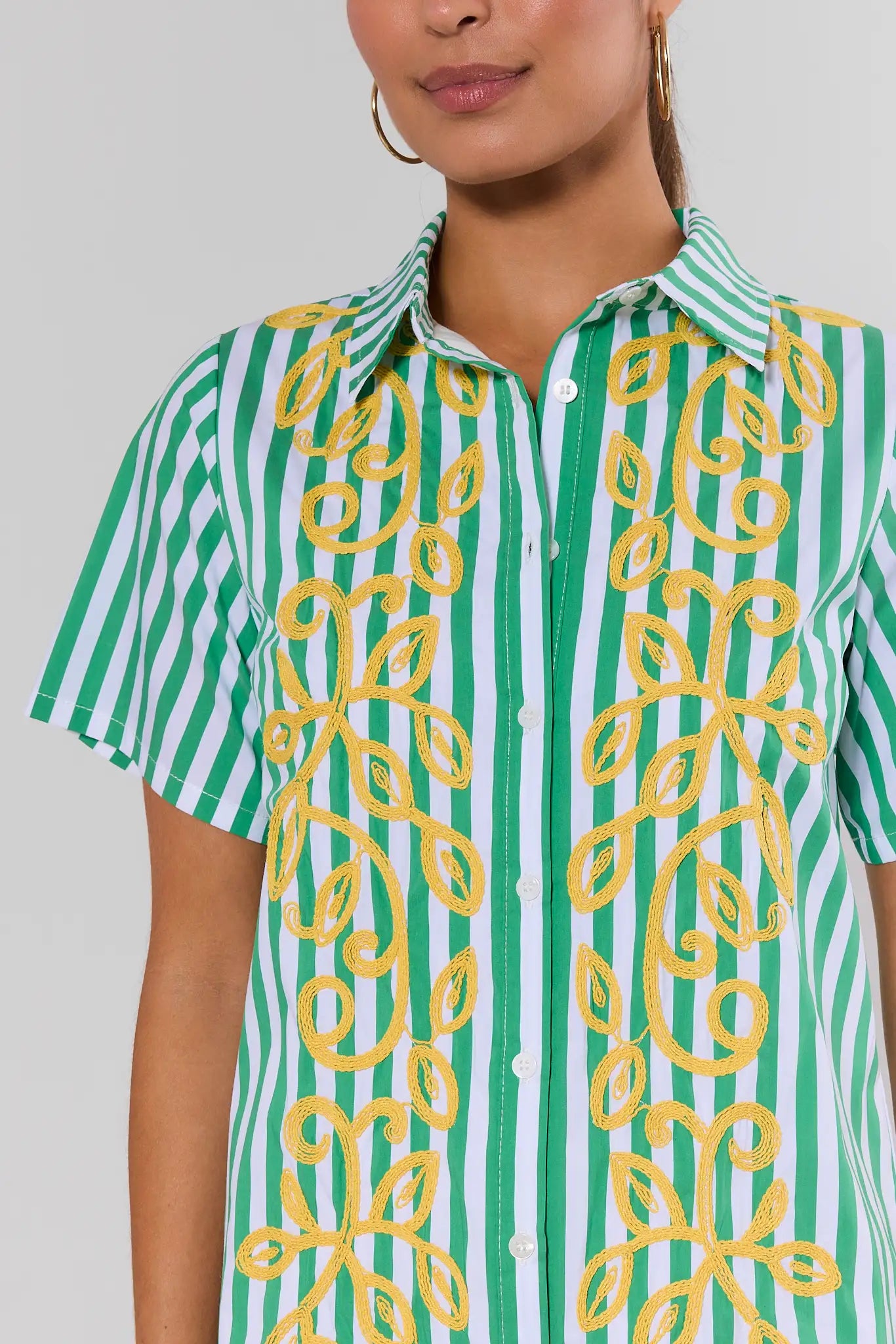 Person wearing a green and white striped shirt with yellow floral patterns on a plain background close