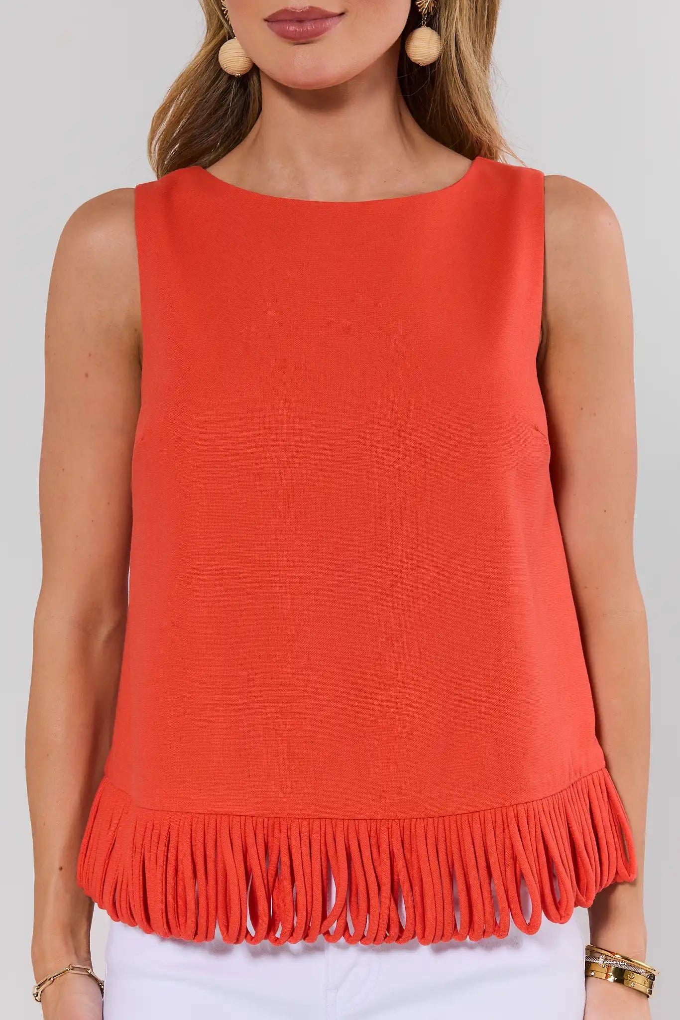 Red sleeveless top with fringe detail worn by a person on a white background close up