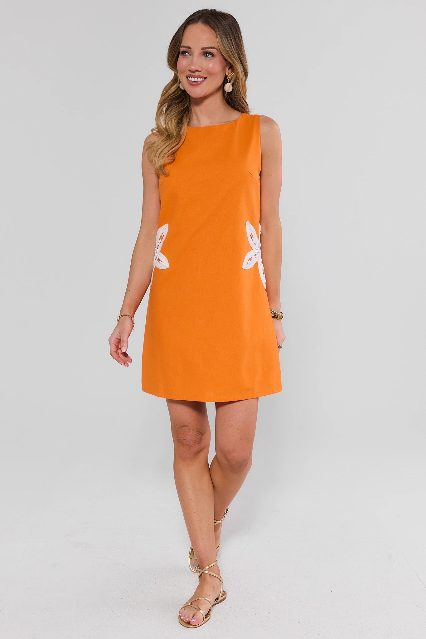 Woman wearing an orange dress with white floral patterns on a white background