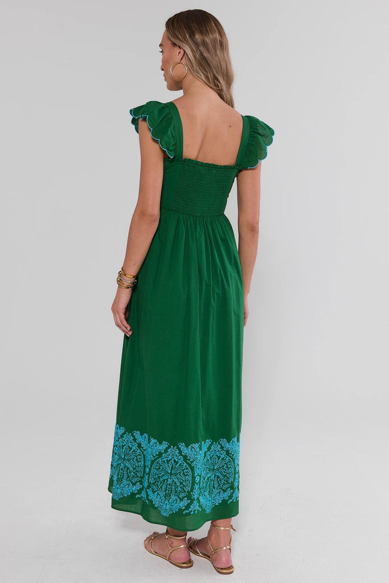 Woman standing wearing a green dress with blue lace details on a white background 