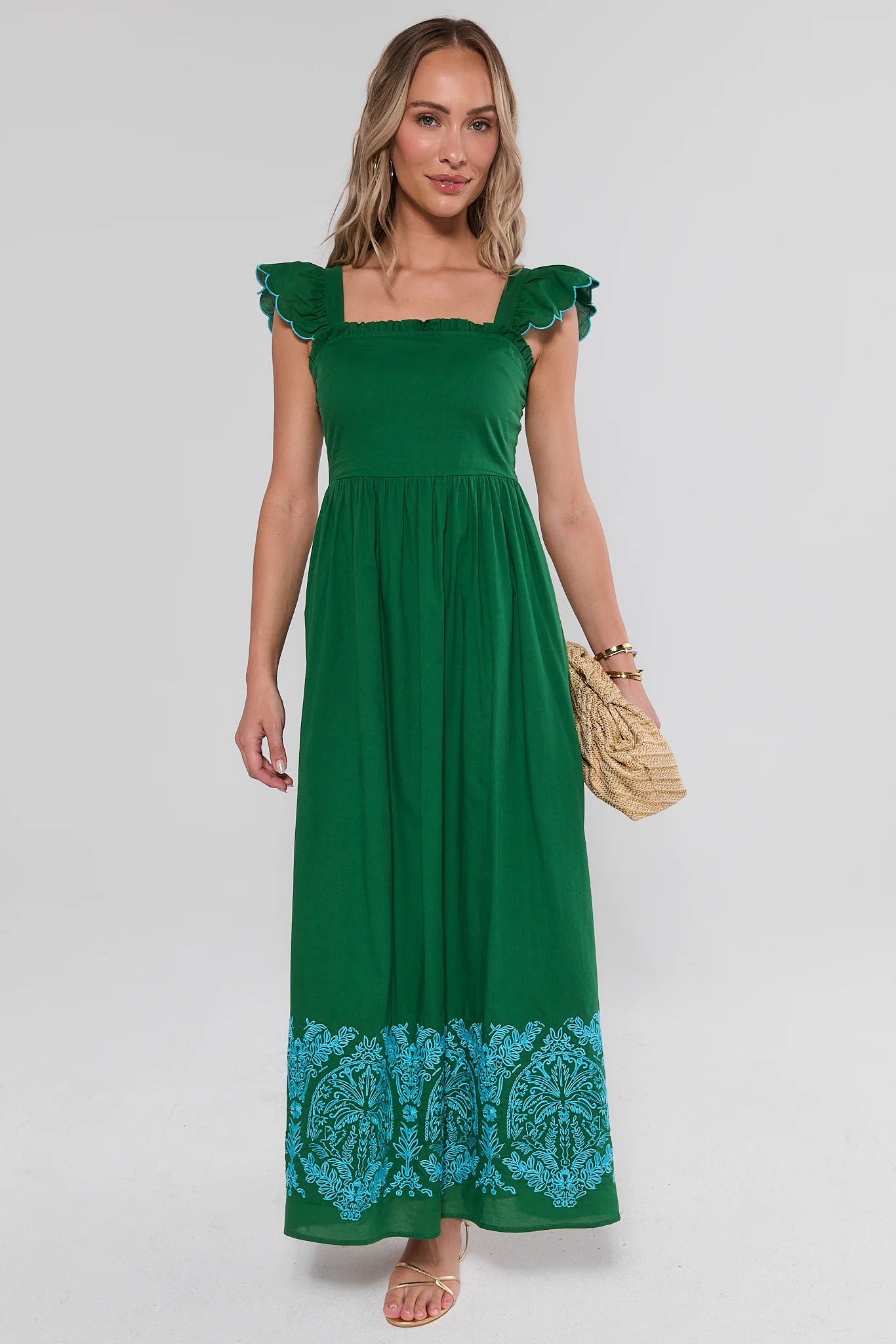 Woman wearing a green dress with floral hem on a white background standing
