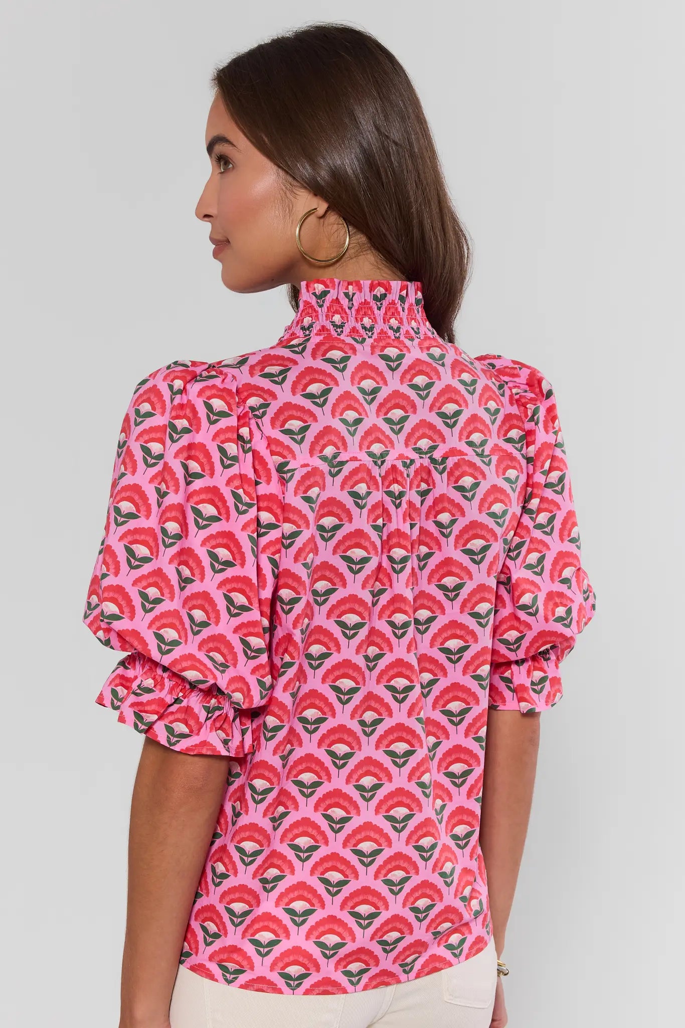 Woman wearing a pink patterned blouse against a plain background stand