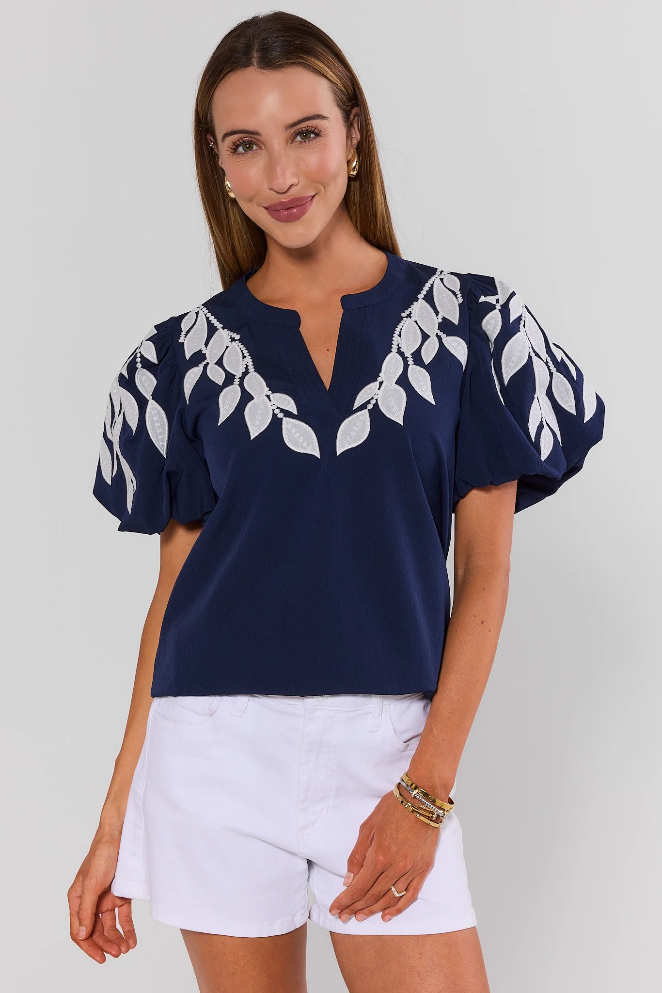 Woman wearing a navy blue top with white leaf patterns and white shorts on a plain background