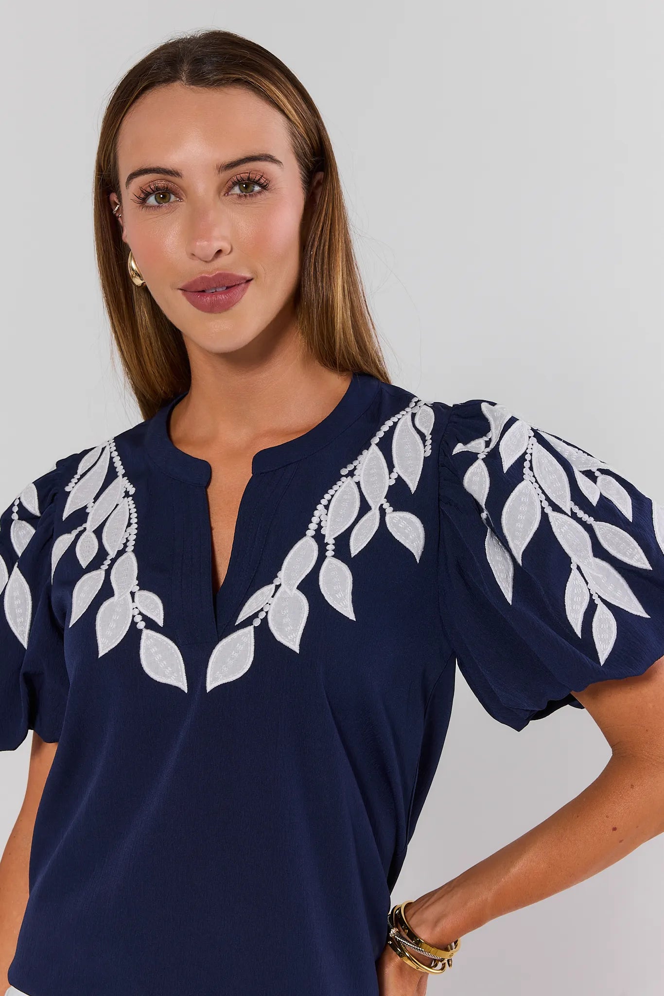 Woman wearing a navy blue top with white leaf patterns on a plain background close up