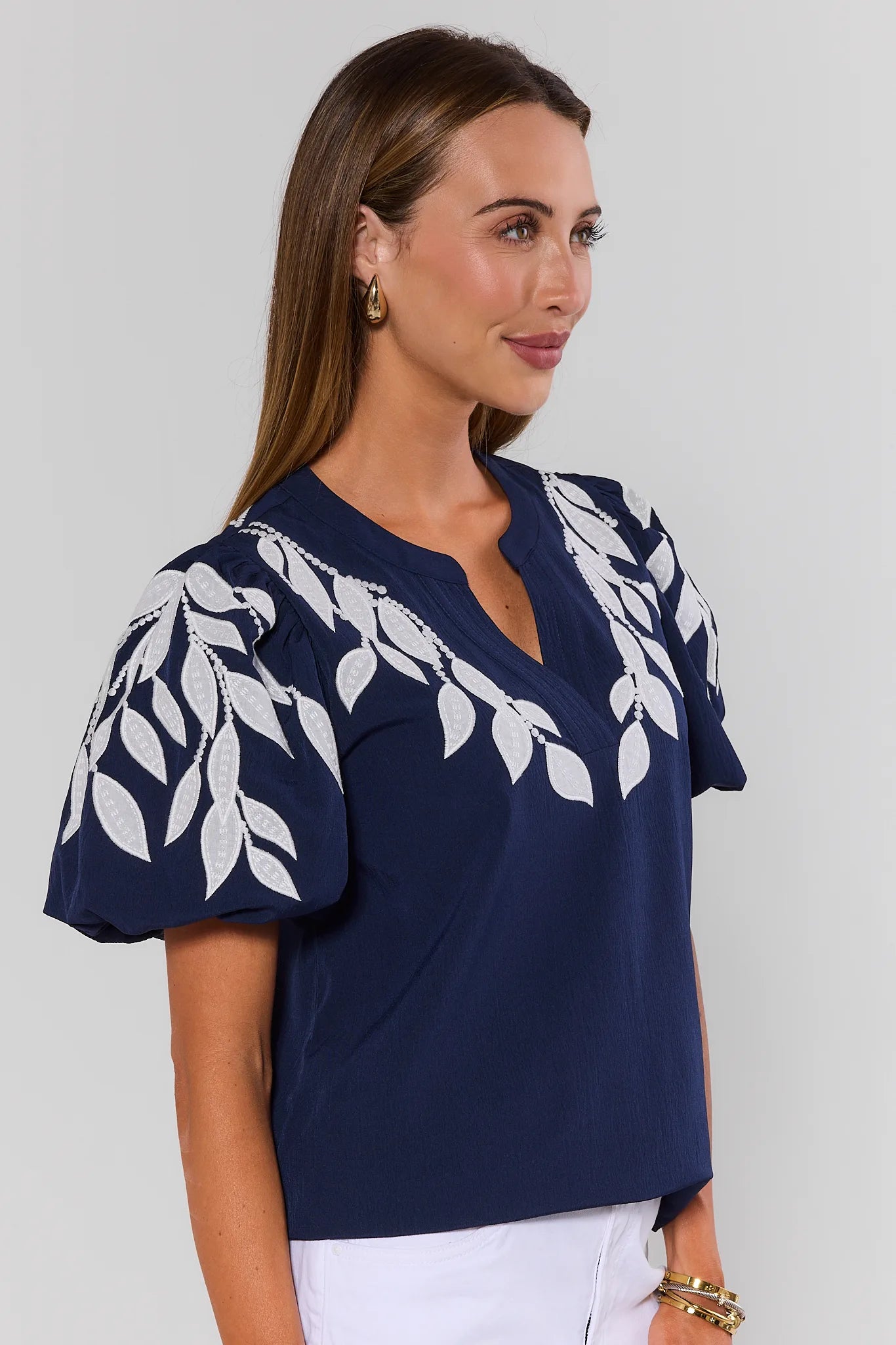 Woman wearing a navy blue top with white leaf patterns on a plain background side
