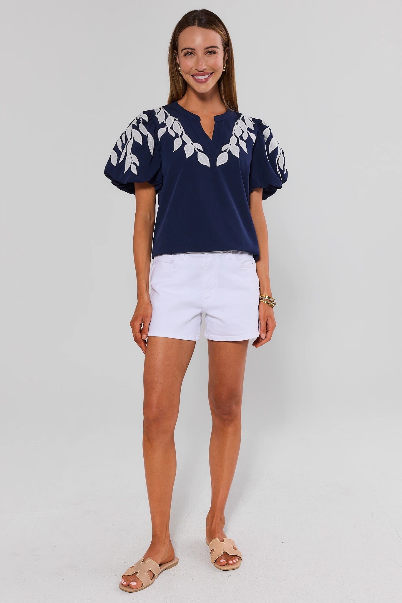 Woman wearing a navy blue top with white floral patterns and white shorts on a light gray background