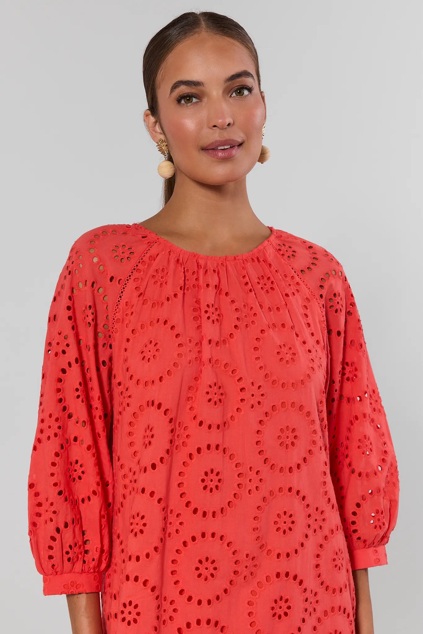 Woman wearing a coral dress with intricate cut-out pattern on a gray background close up