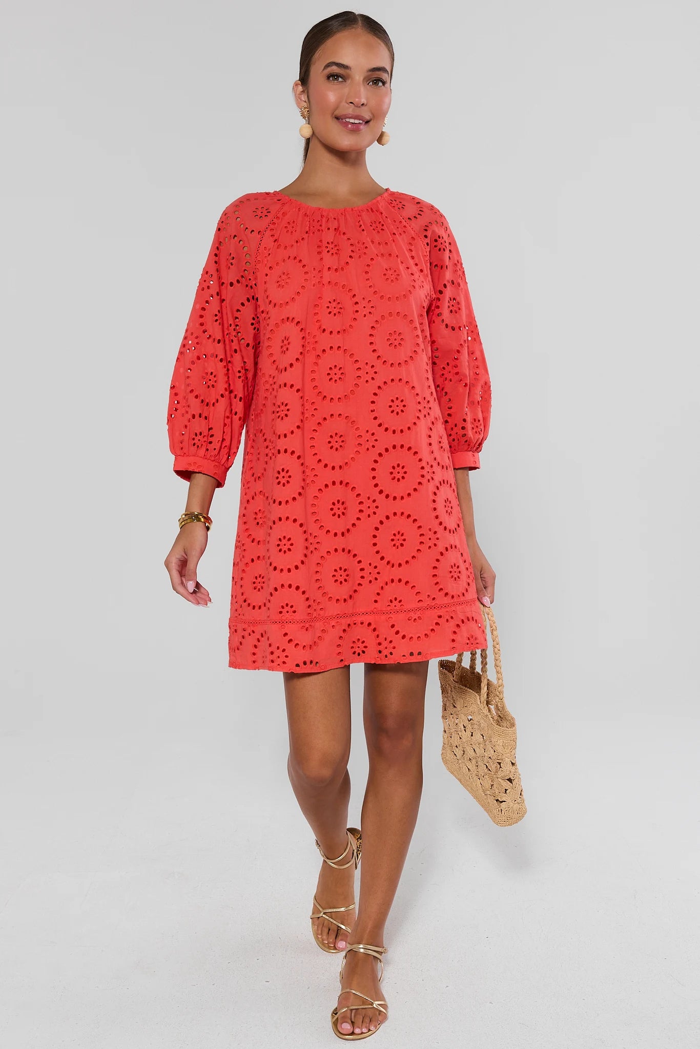 Woman wearing a red lace dress holding a straw bag on a white background walking