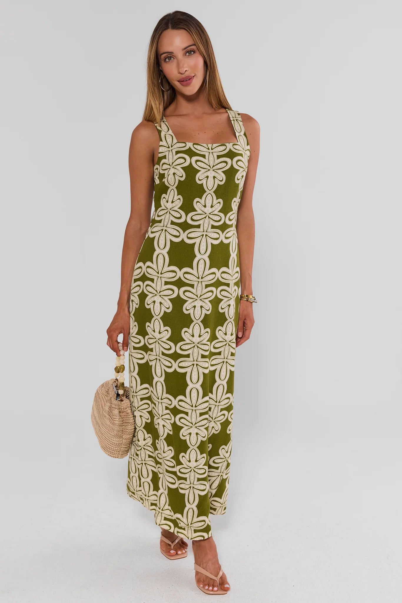 Woman wearing a green and white patterned dress holding a straw bag on a white background walking