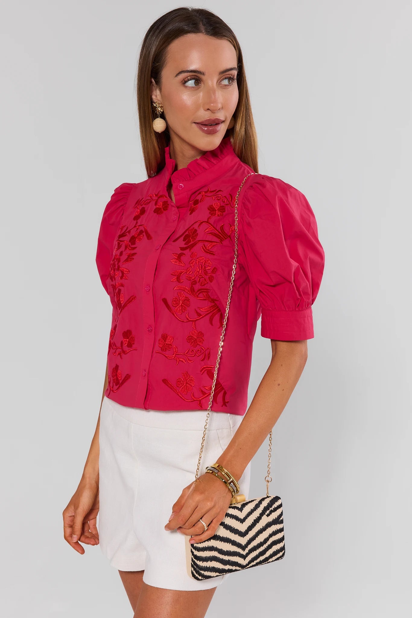 Woman wearing a pink blouse with floral embroidery and white shorts, holding a zebra-striped handbag.