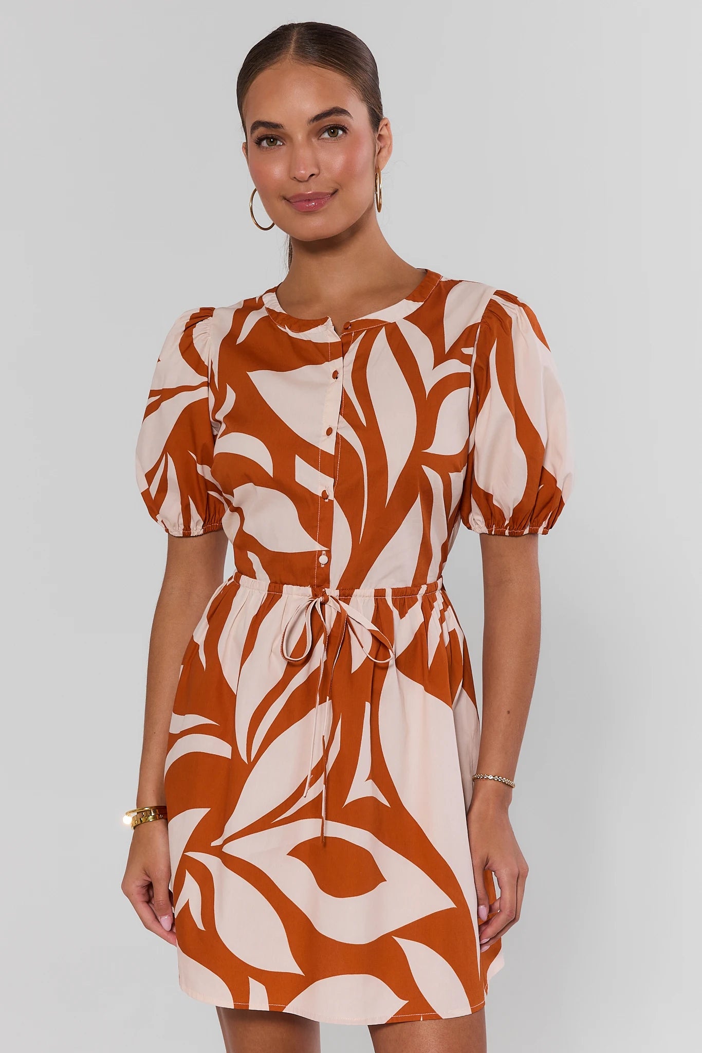 Woman wearing a brown and white patterned dress on a plain background