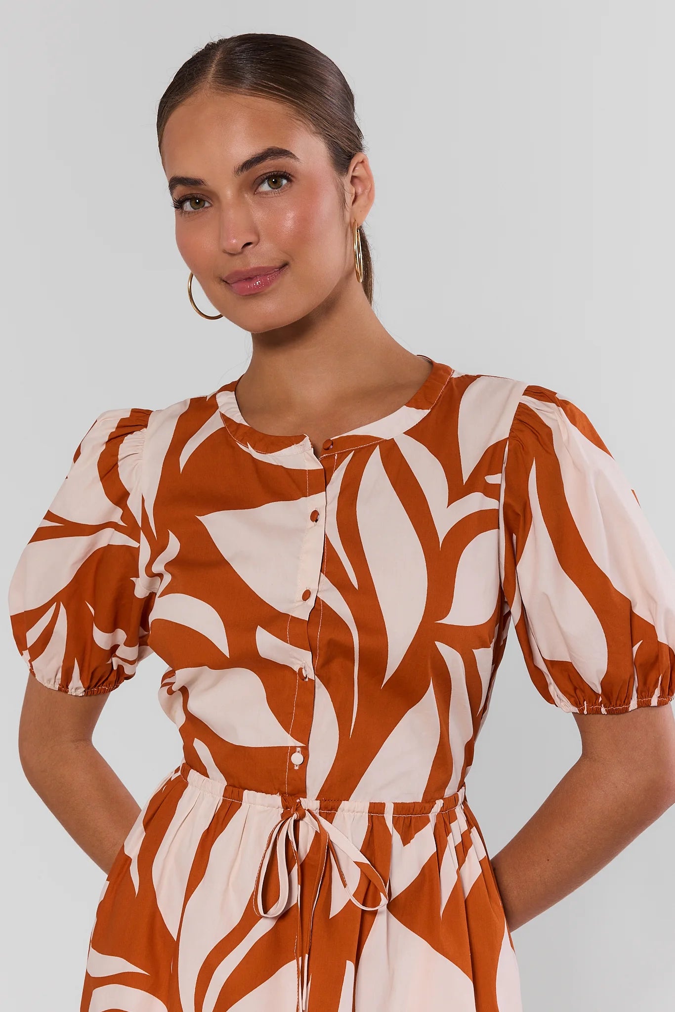Woman wearing a brown and white patterned dress against a plain background close up