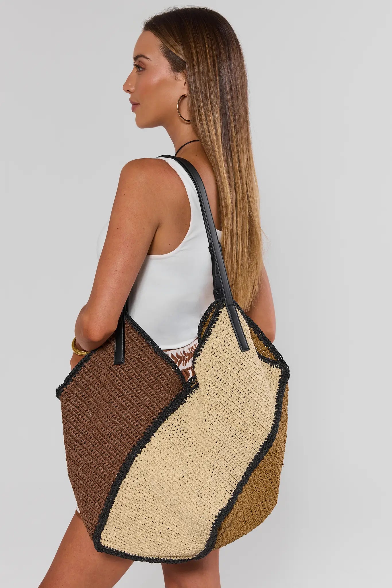 Woman carrying a two-tone woven bag with brown and beige sections on a plain background