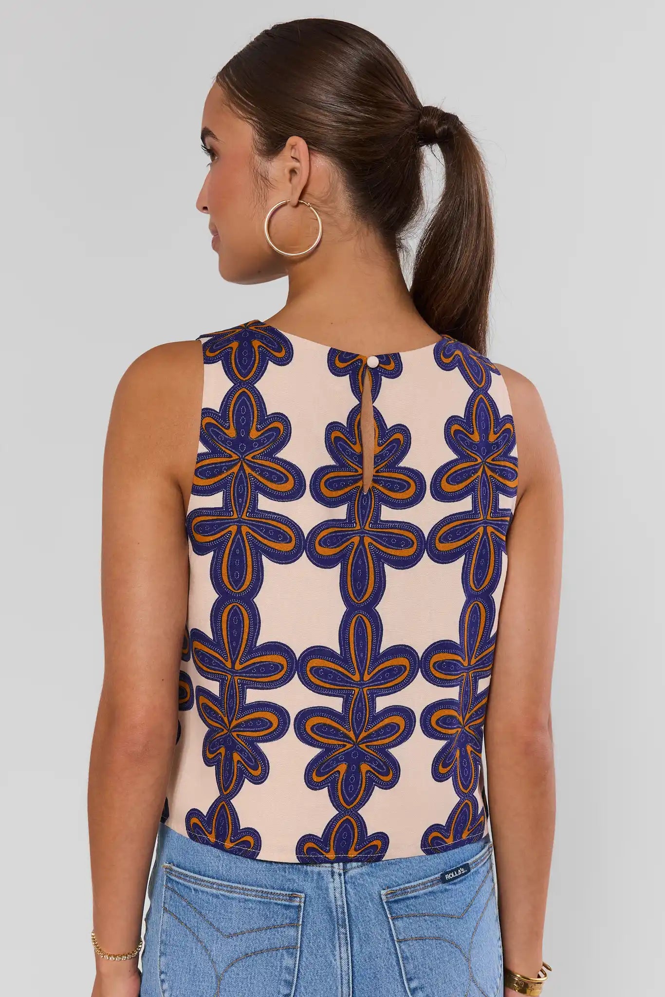 Woman standing wearing a sleeveless top with a geometric pattern on a plain background