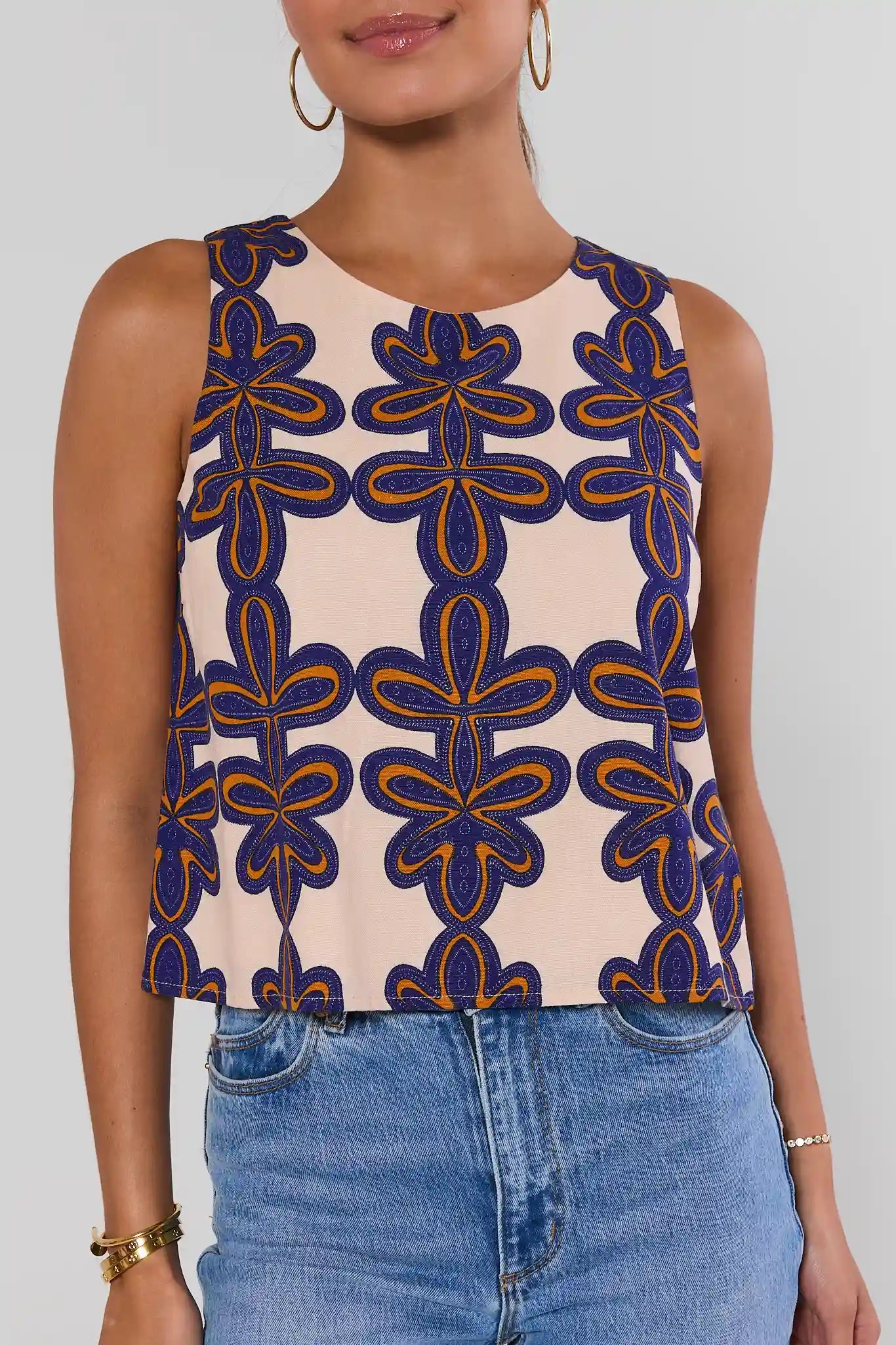 Woman wearing a sleeveless top with a blue and orange floral pattern on a plain background close up
