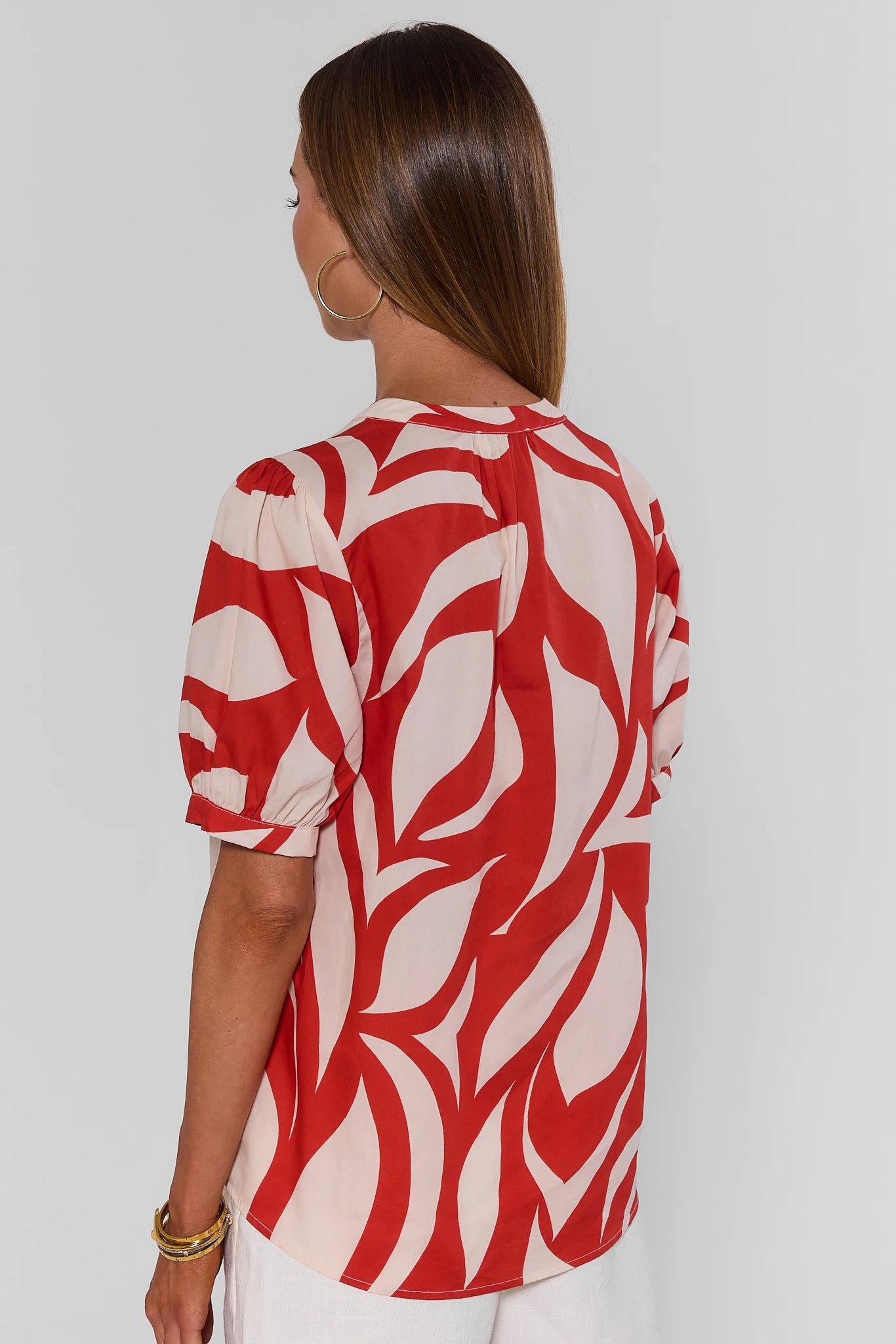 Woman standing wearing a red and white patterned blouse against a plain background