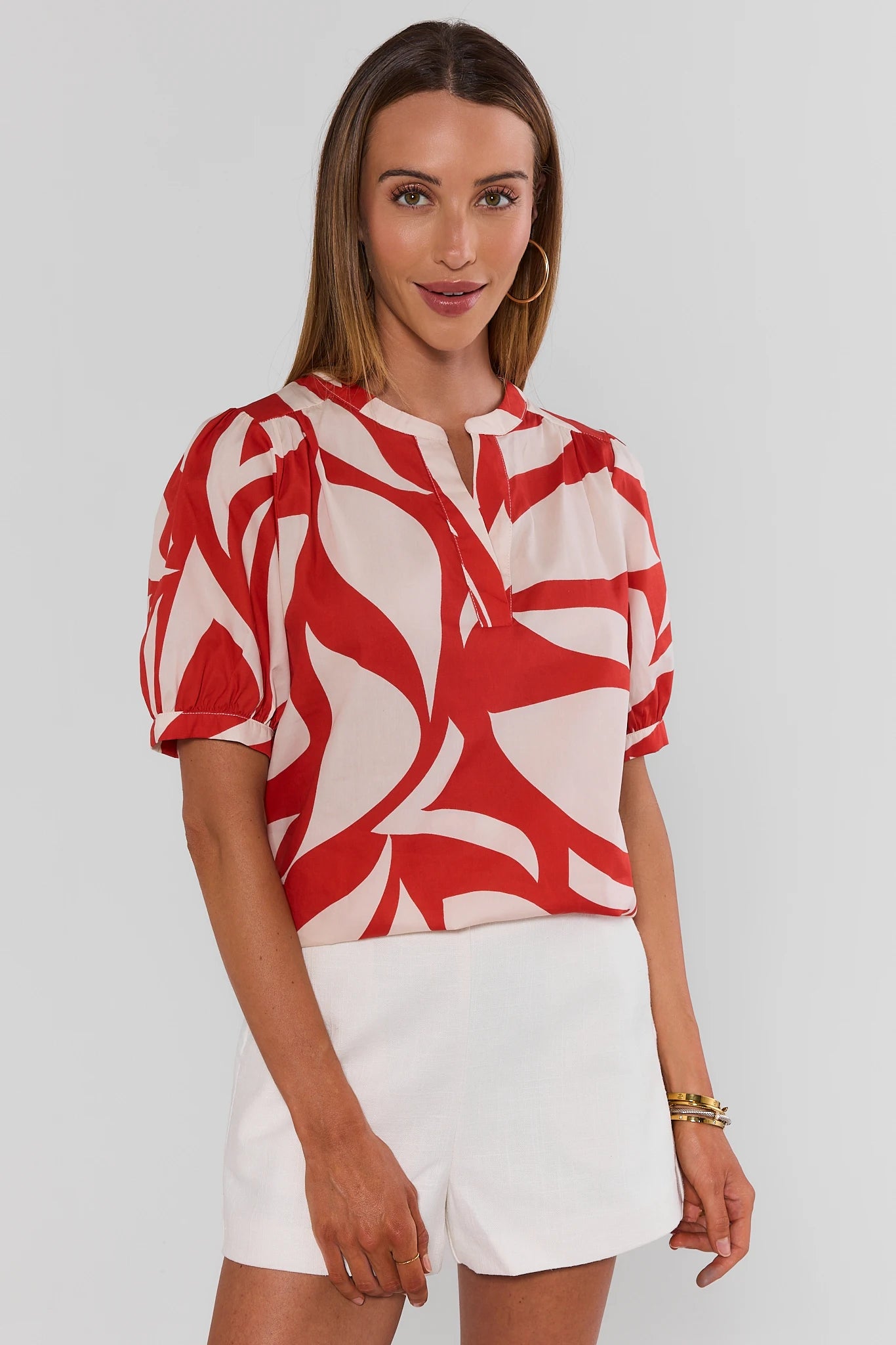 Woman wearing a red and white patterned blouse with white shorts on a plain background