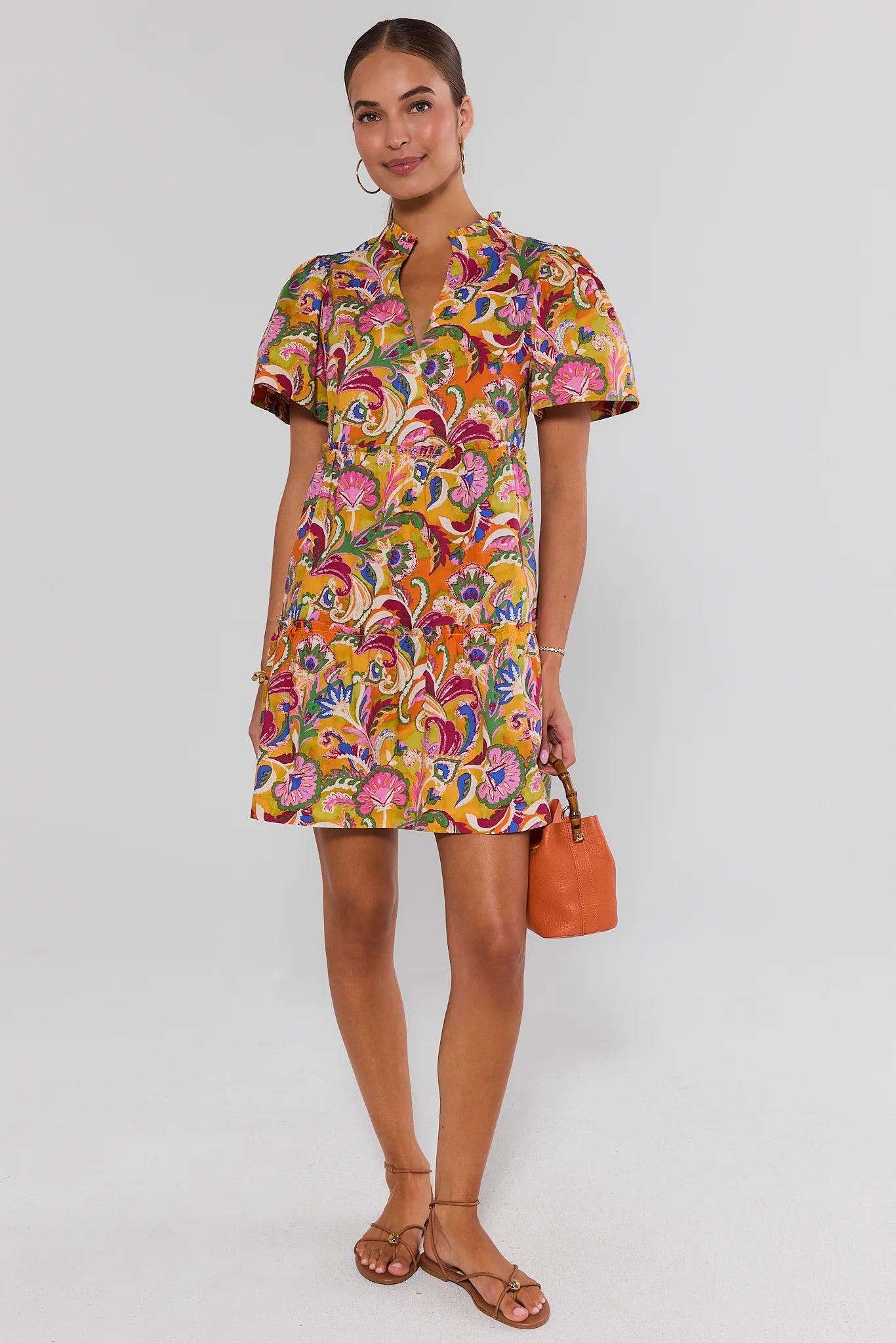 Woman wearing a colorful patterned dress holding an orange handbag on a white background standing