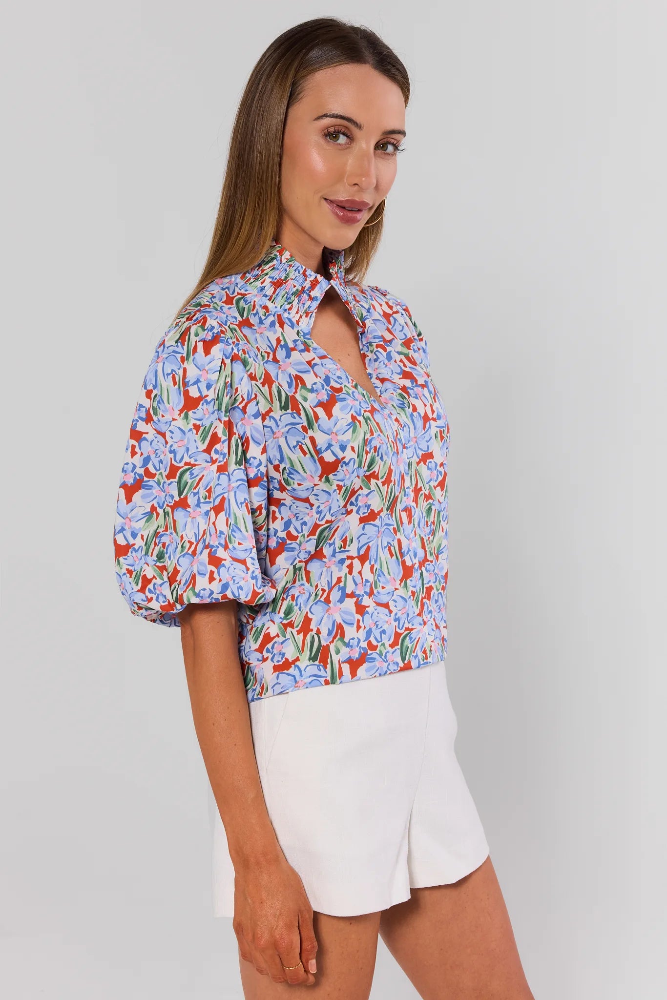 Woman wearing a colorful floral blouse and white shorts on a plain background side