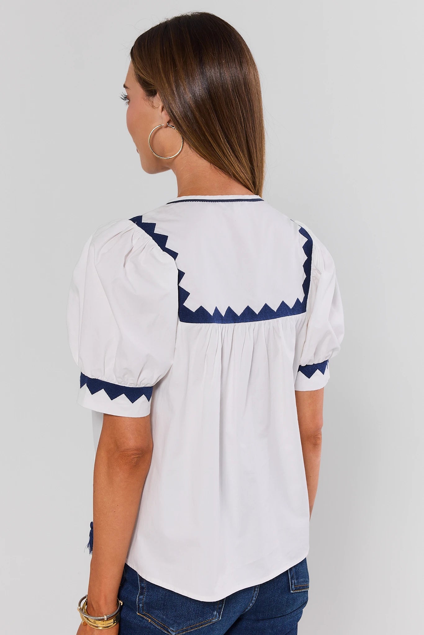 Woman standing wearing a white blouse with blue accents on a plain background