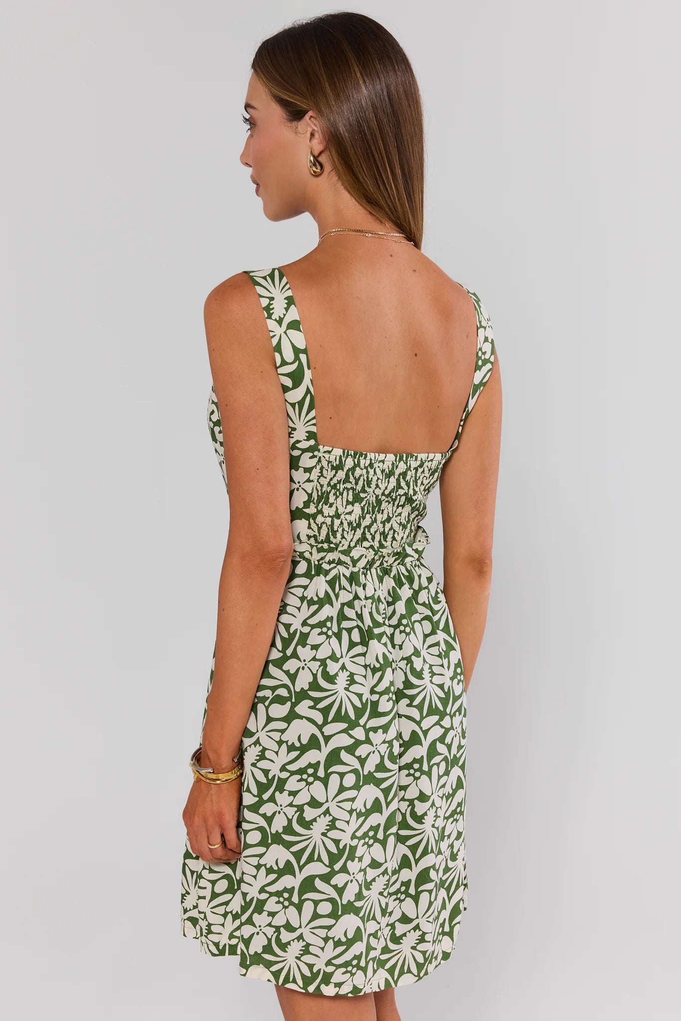 Woman wearing a green and white patterned dress on a plain background standing