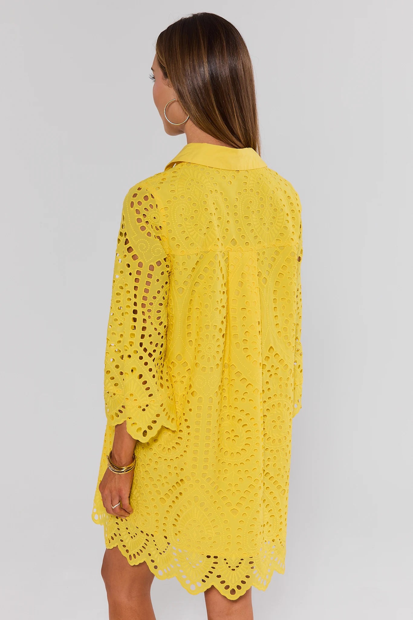 Woman standing wearing a yellow lace dress against a plain background