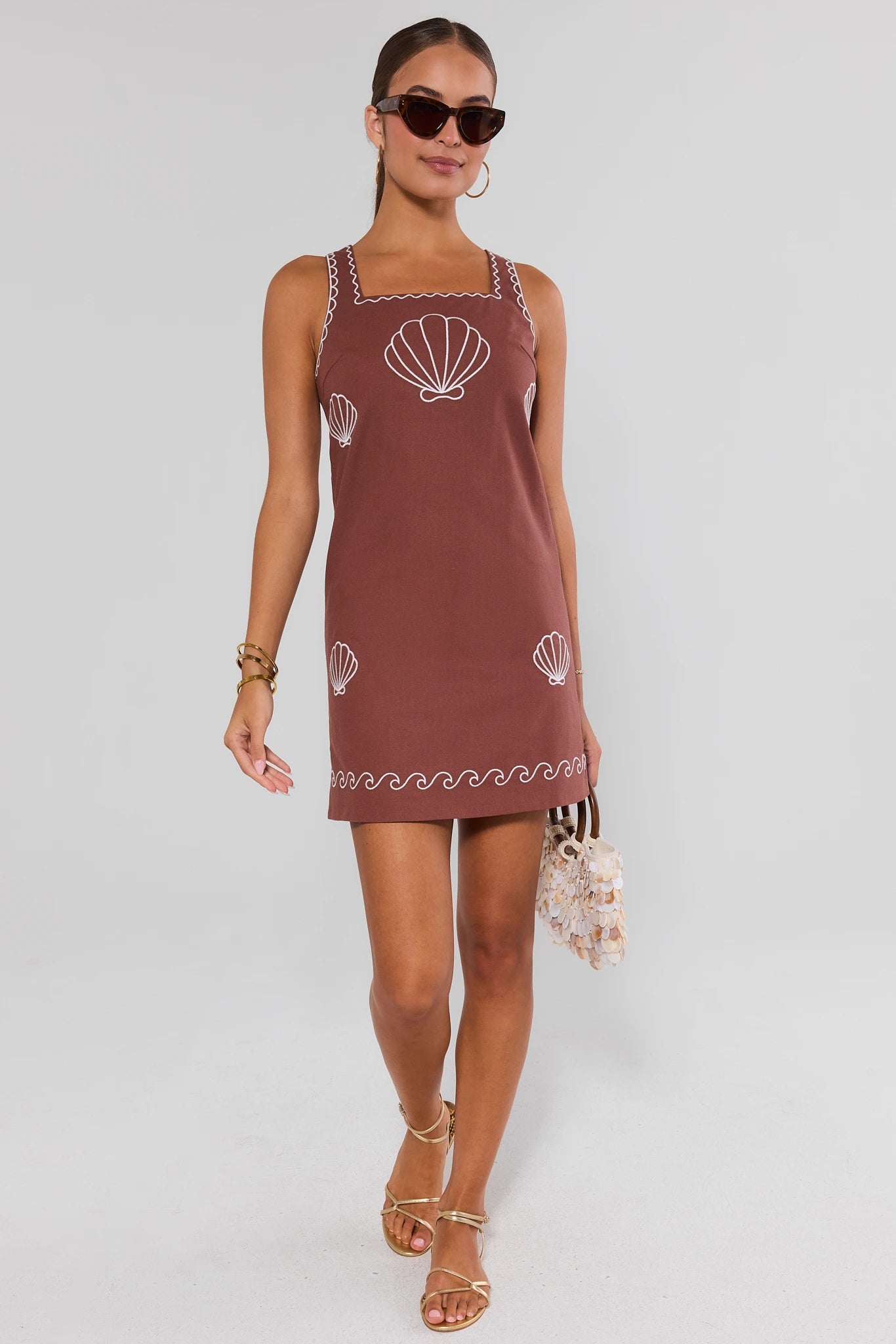 Woman wearing a brown dress with shell patterns on a white background walking