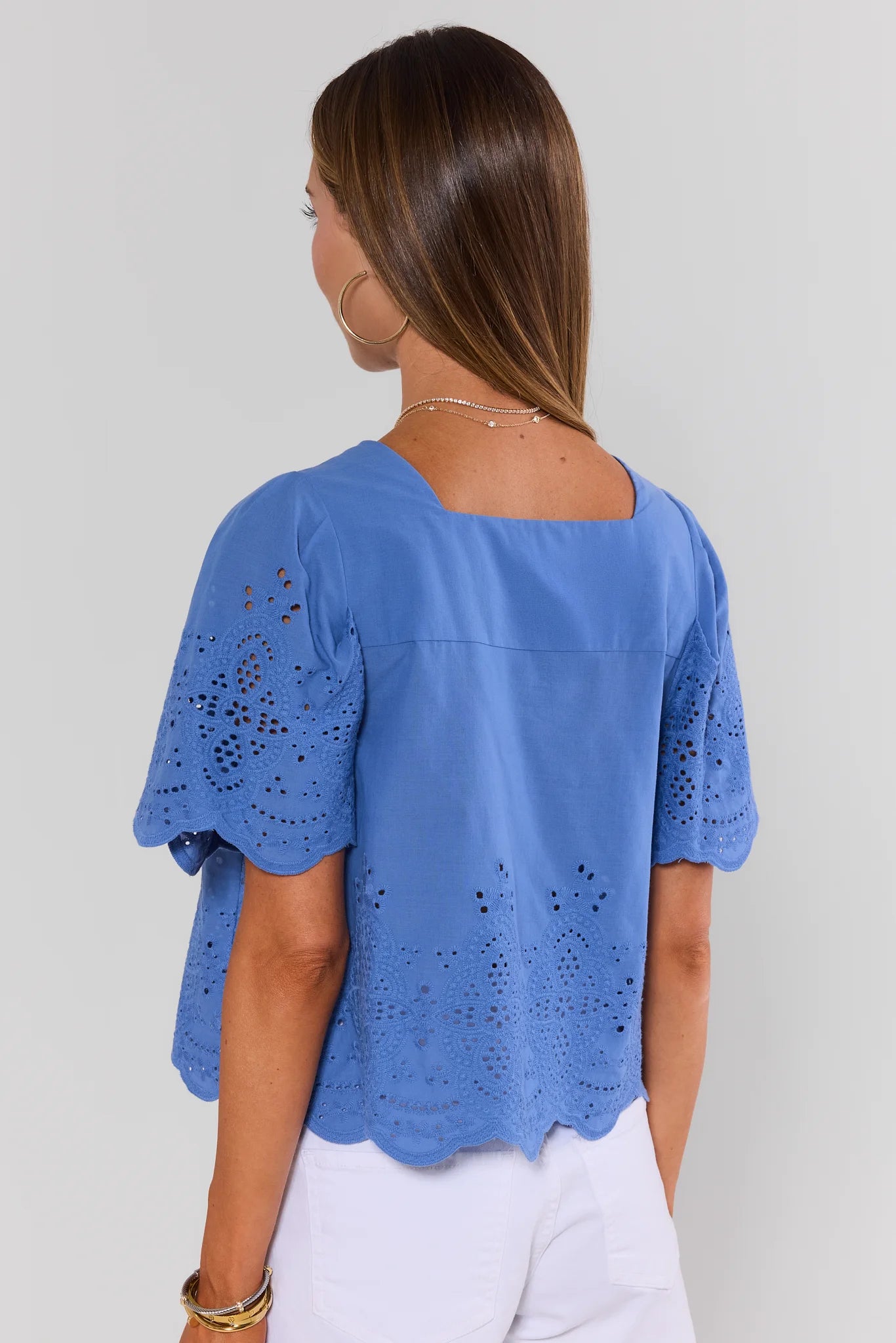 Woman standing wearing a blue blouse with cut-out sleeves on a plain background