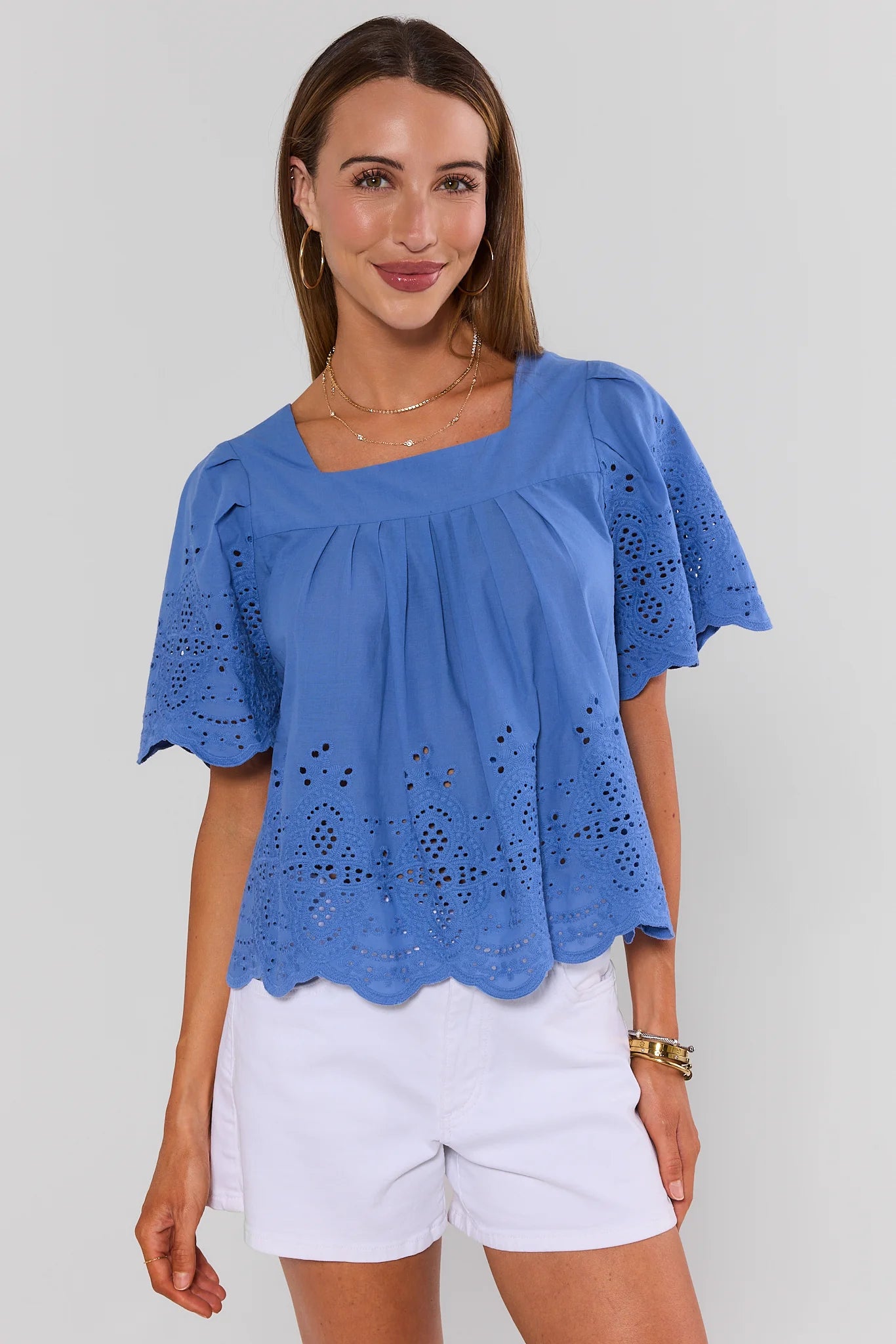 Woman wearing a blue blouse with cut-out details and white shorts on a plain background