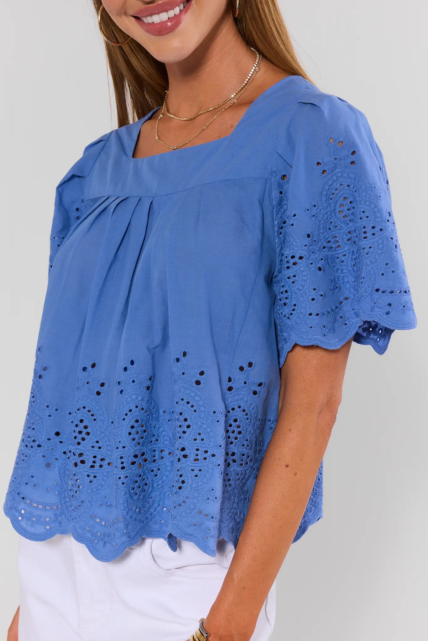 Woman wearing a blue blouse with intricate cut-out patterns on a plain background close up