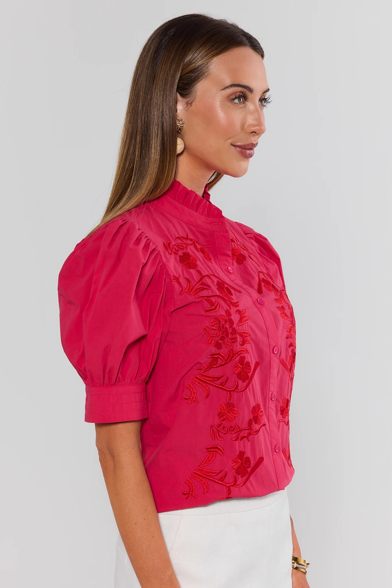 Woman wearing a pink blouse with hot pink embroidery on a white background side