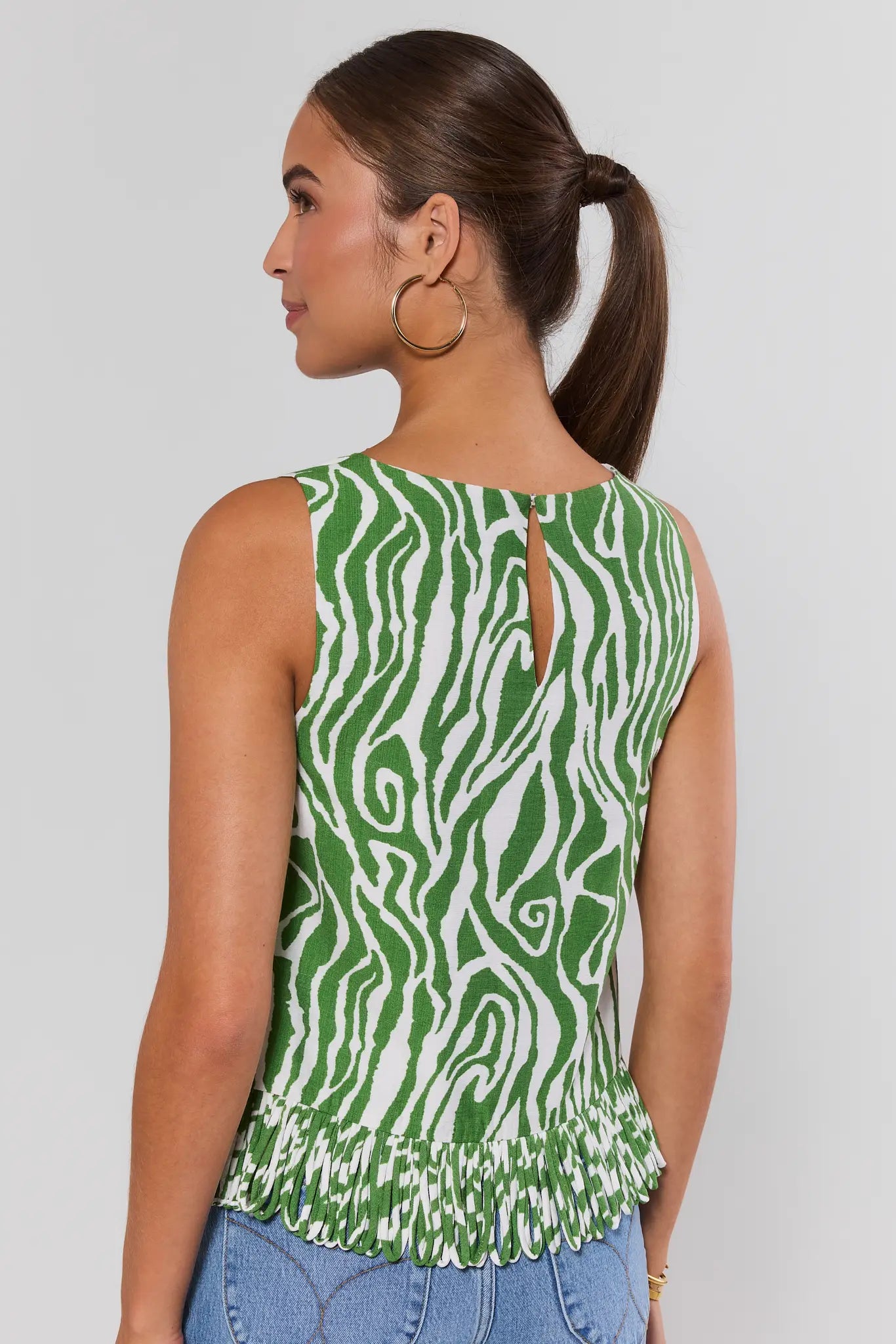 Woman standing wearing a green and white patterned sleeveless top with a plain background