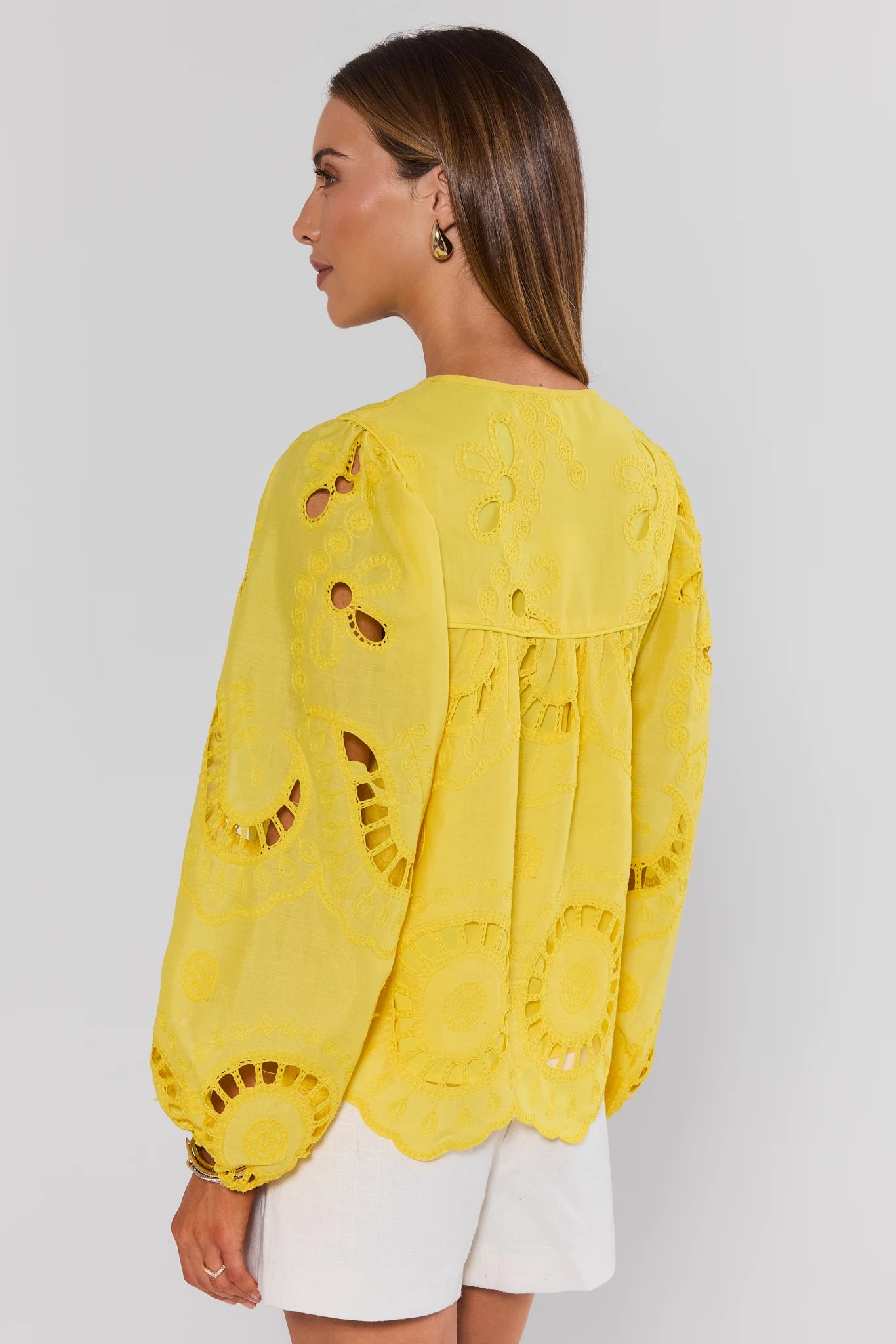 Woman standing wearing a yellow lace top against a white background
