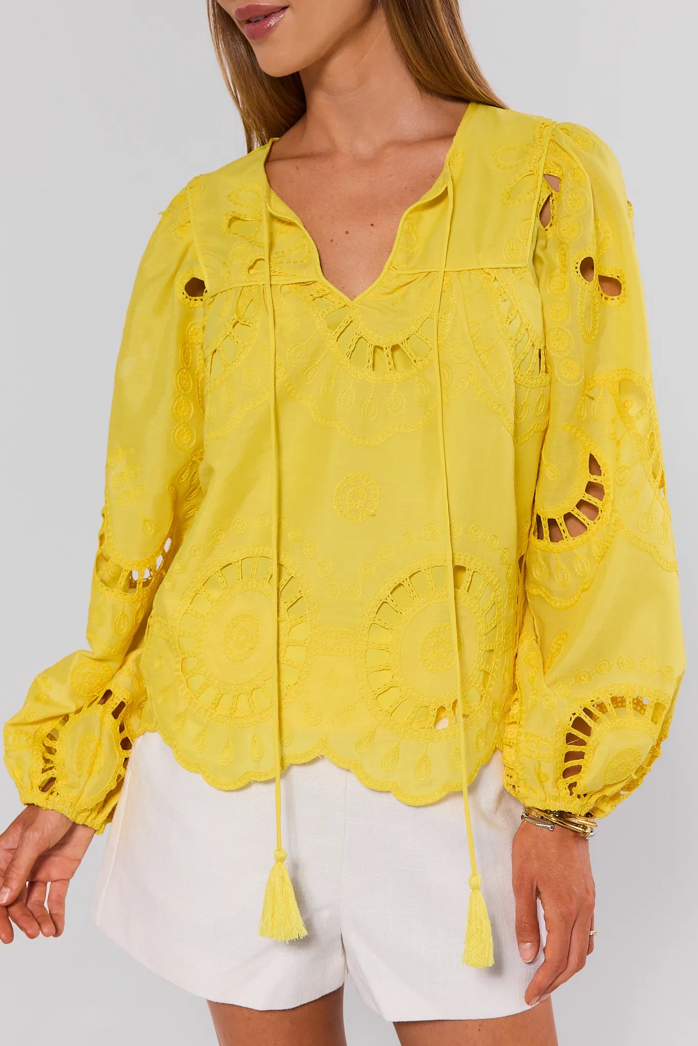 Yellow embroidered blouse worn by a person on a light gray background close up