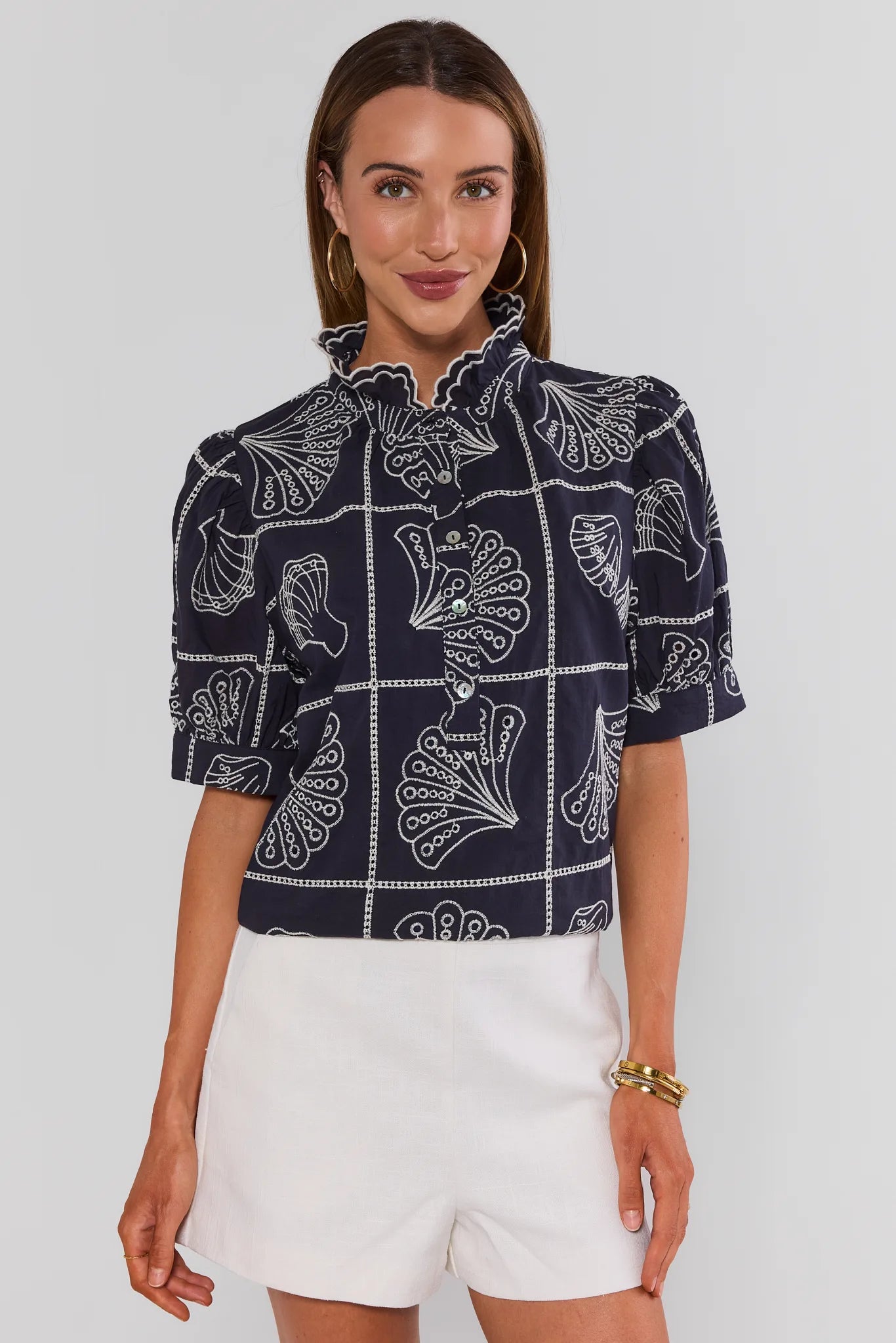 Woman wearing a navy patterned shirt and white shorts on a light gray background