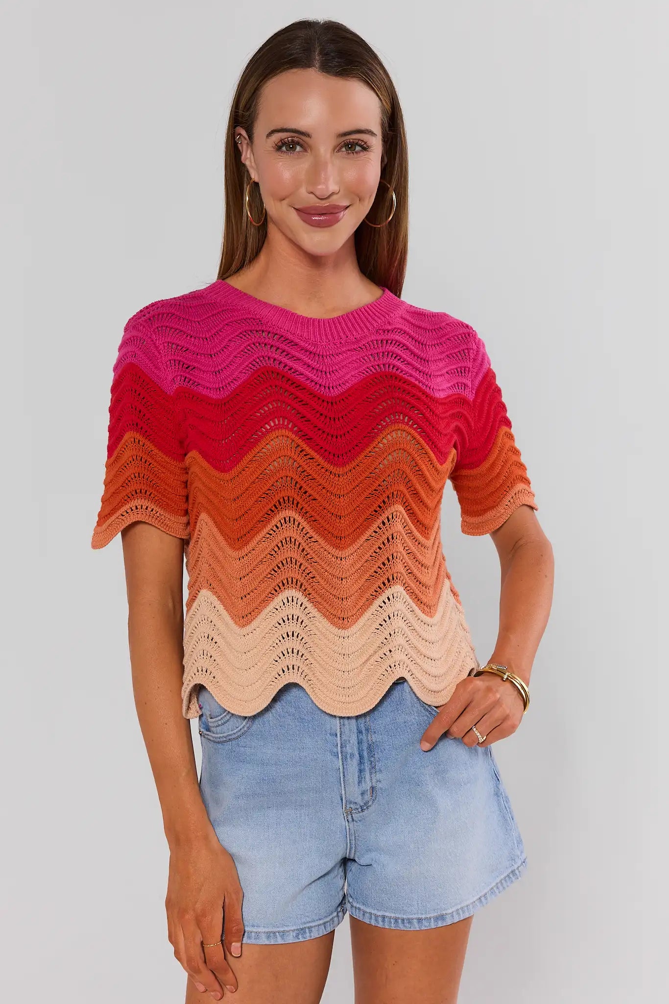 Woman wearing a colorful knit sweater and denim shorts on a plain background