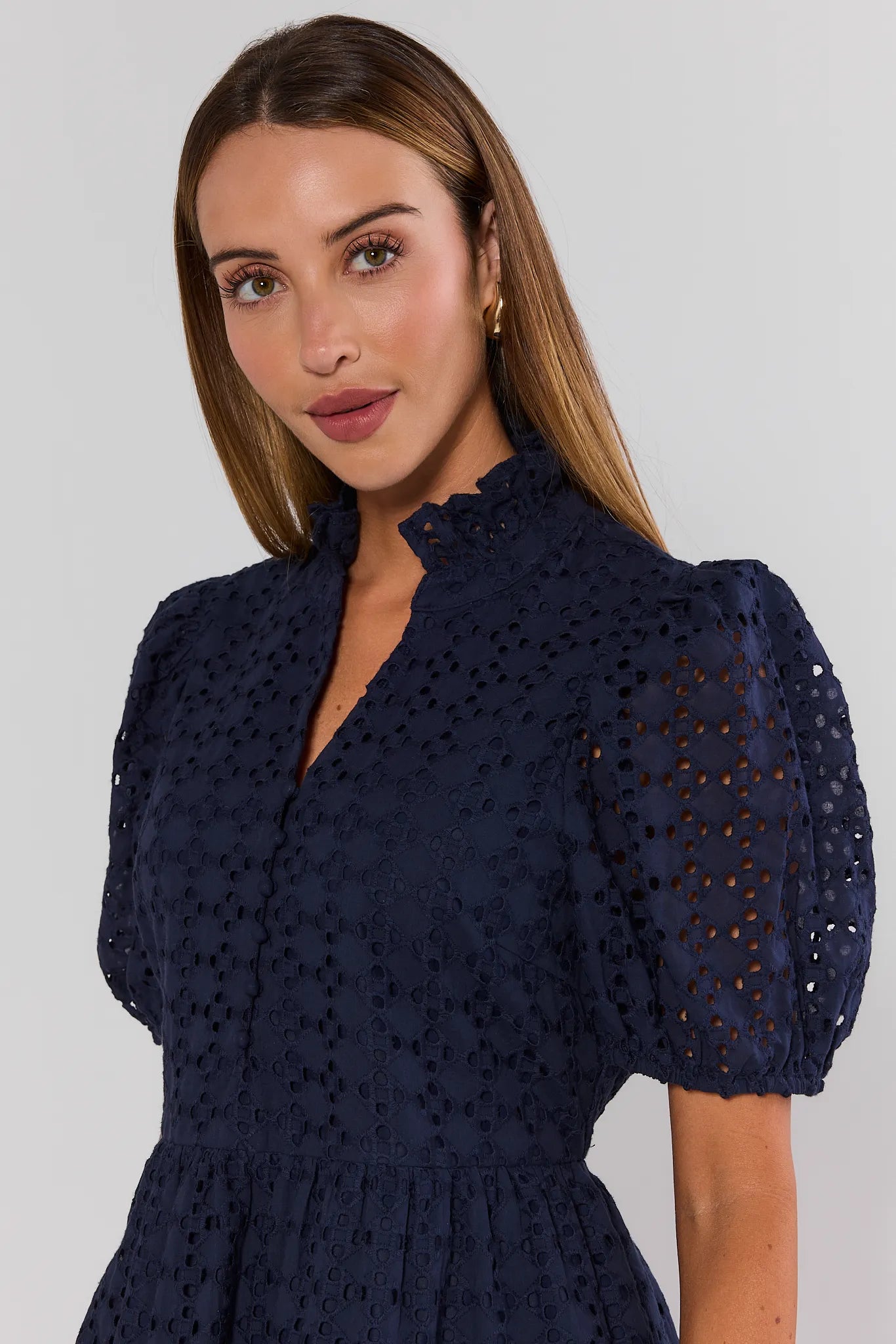 Woman wearing a navy blue dress with puff sleeves against a plain background close up