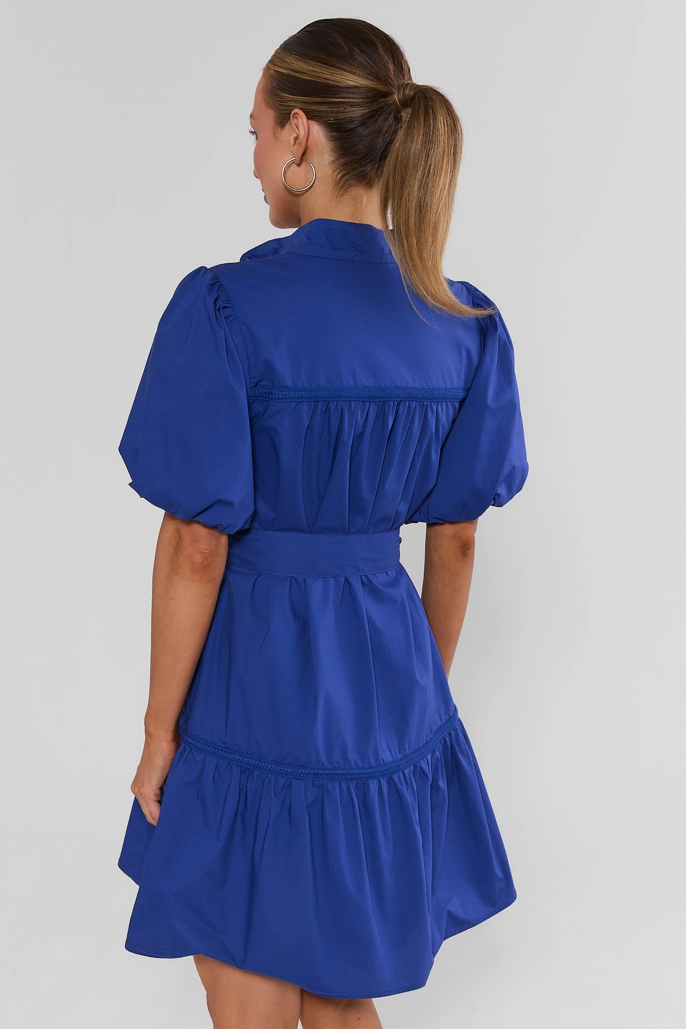Woman standing wearing a blue dress with puff sleeves on a plain background