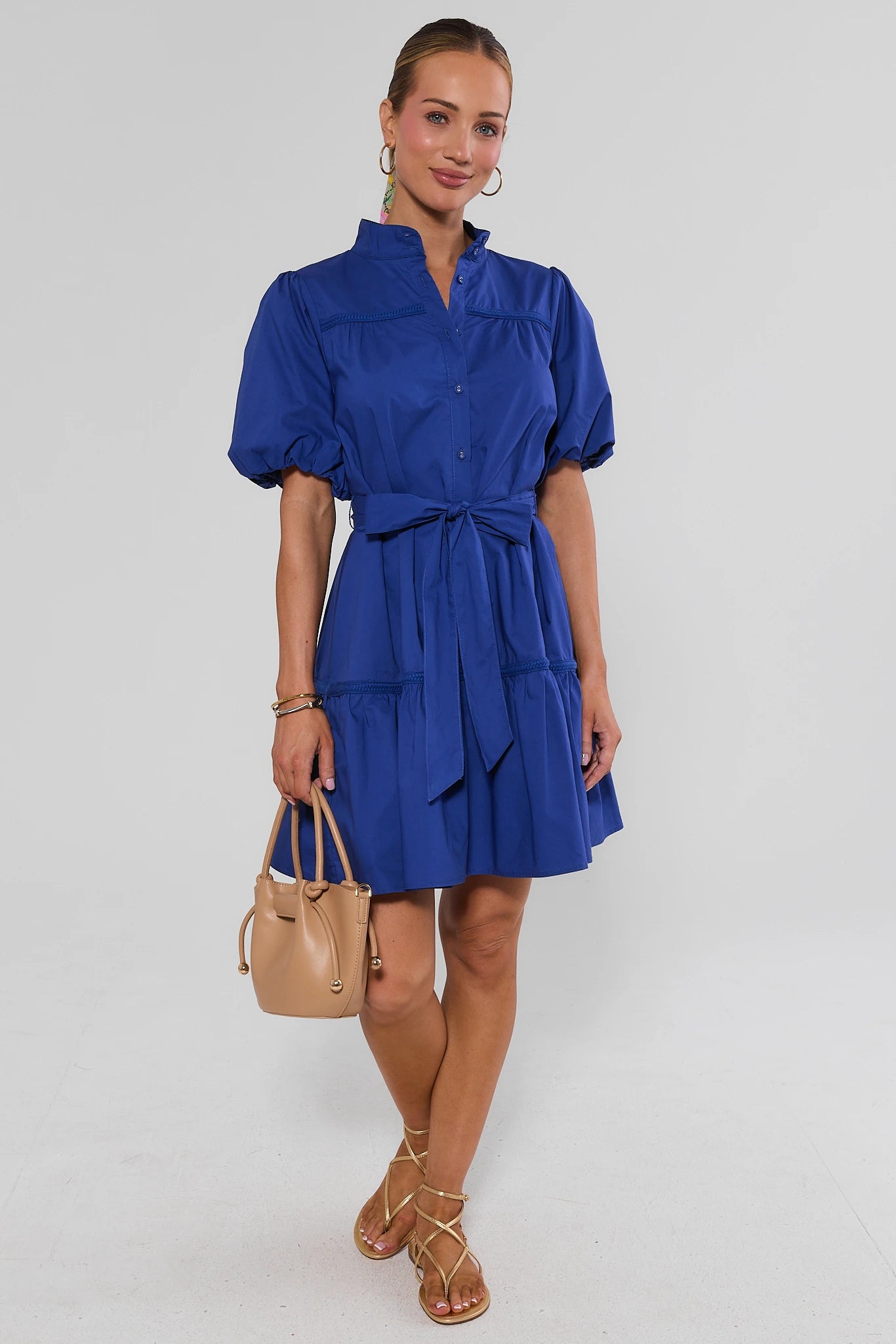 Woman wearing a blue dress with a beige handbag on a white background walking
