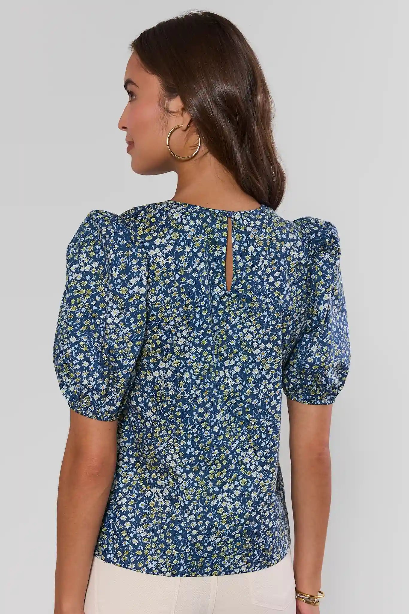 Woman wearing a blue floral blouse with puff sleeves on a plain background side