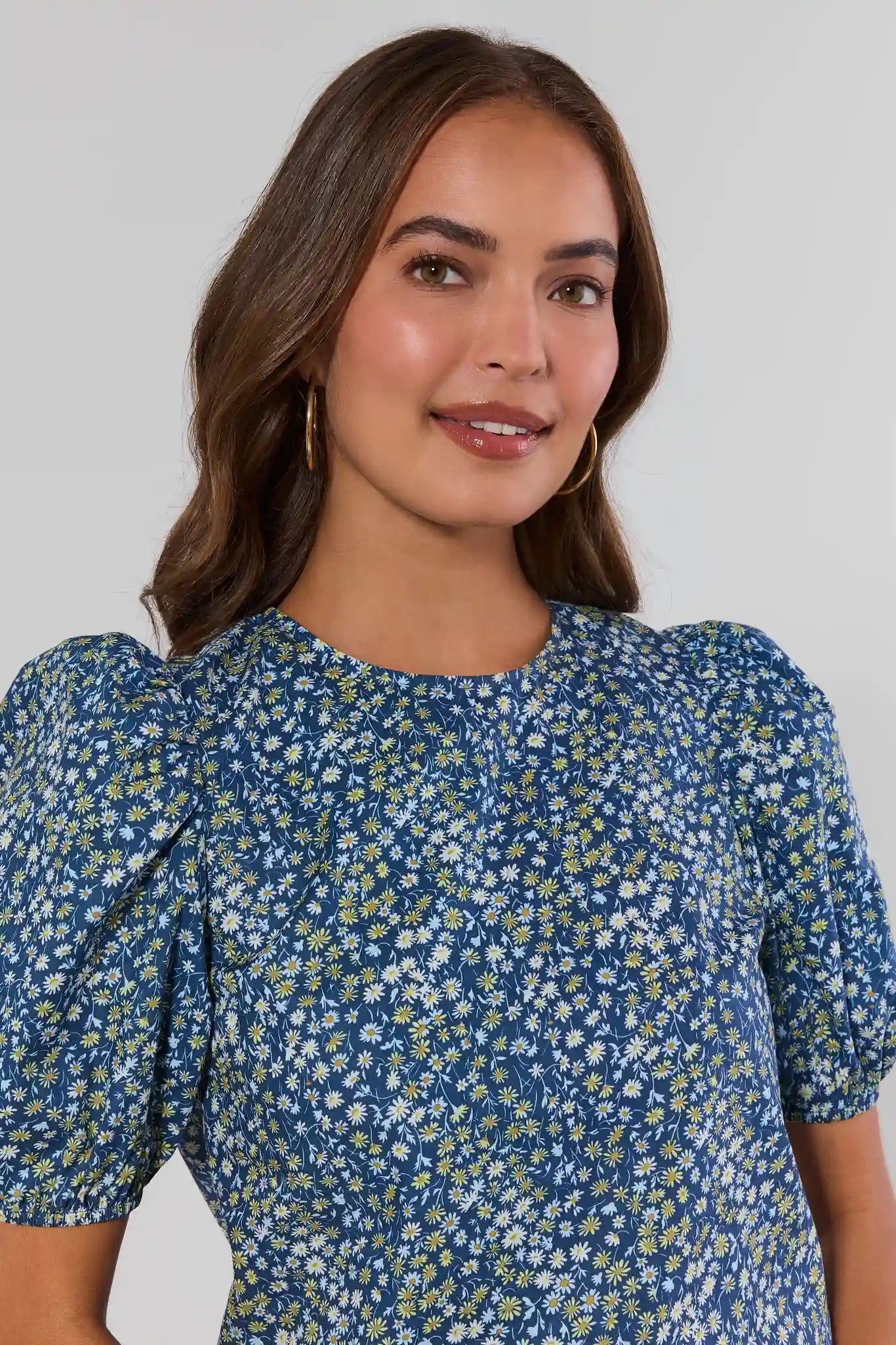 Woman wearing a blue floral dress against a plain background close up