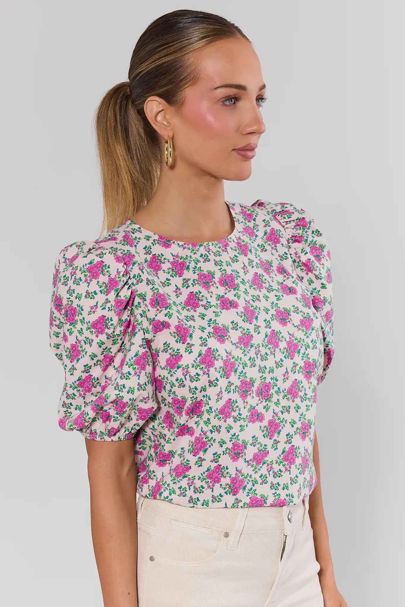 Woman wearing a floral blouse with puff sleeves against a plain background side